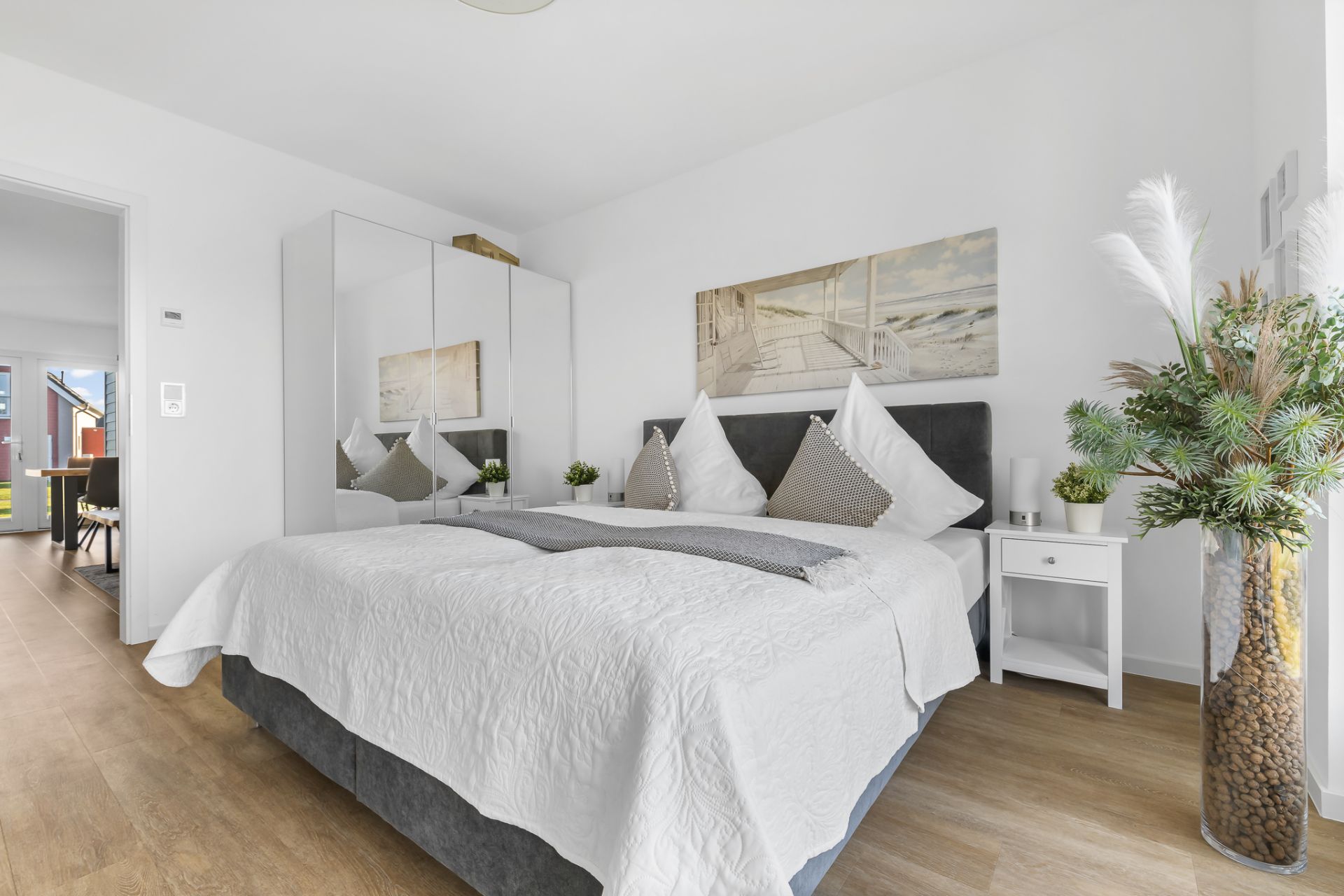 Helles Schlafzimmer mit Doppelbett, Spiegelkleiderschrank, Pflanzen und Wandbild.