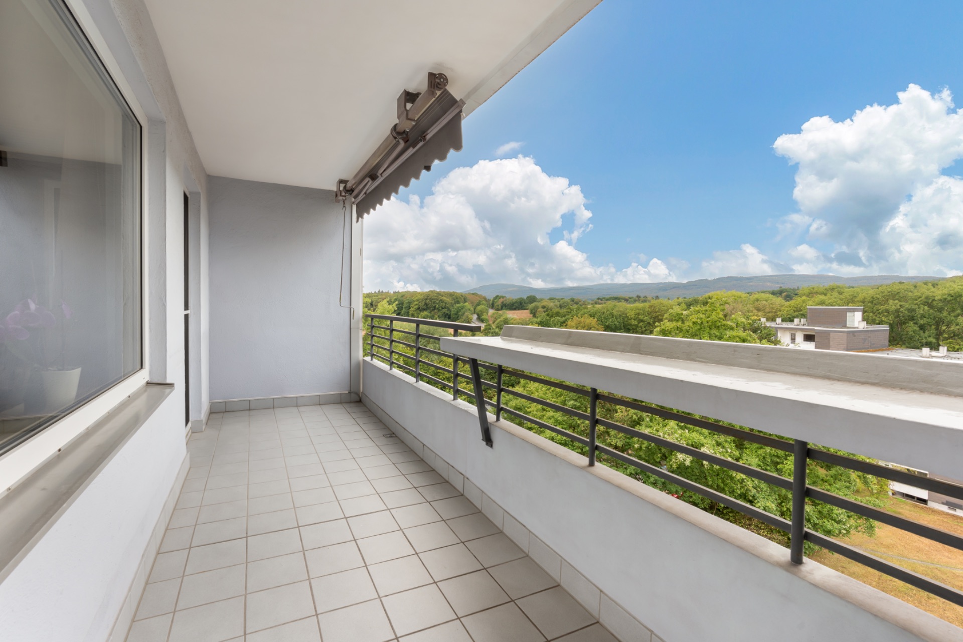 Überdachter Balkon mit Fliesenboden und Aussicht ins Grüne.