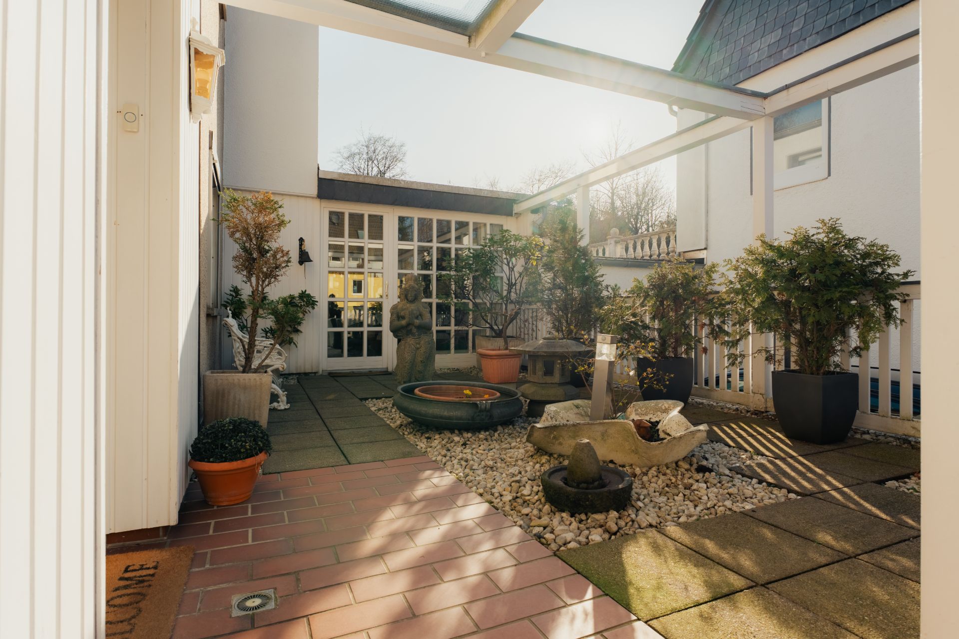 Überdachte Terrasse mit Pflanzkübeln, Brunnen und Steinskulptur im Innenhof.