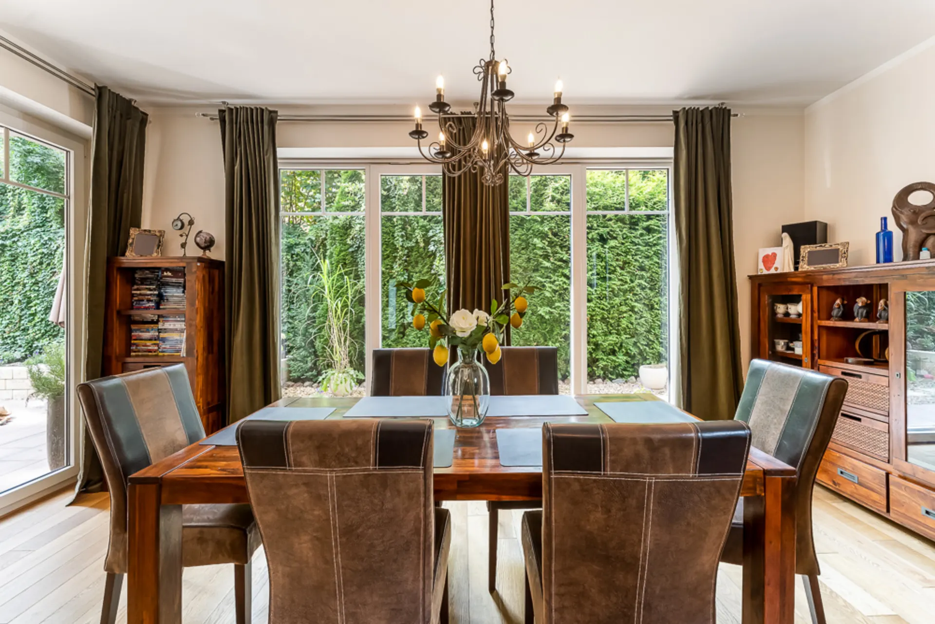 Esszimmer mit Holztisch, sechs Stühlen, Kronleuchter und Blick in den Garten.