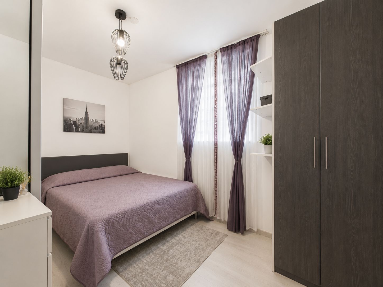 Helles Schlafzimmer mit Doppelbett, Kleiderschrank, Vorhängen und Dekoration.
