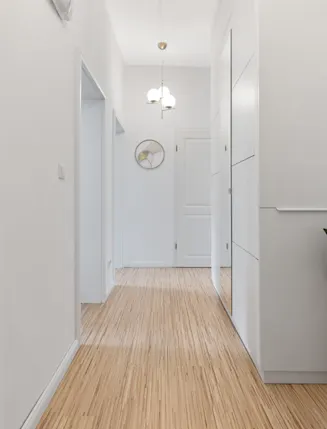 Heller Flur mit Holzboden, weißen Wänden, einem Spiegel und einer grünen Pflanze im Topf.