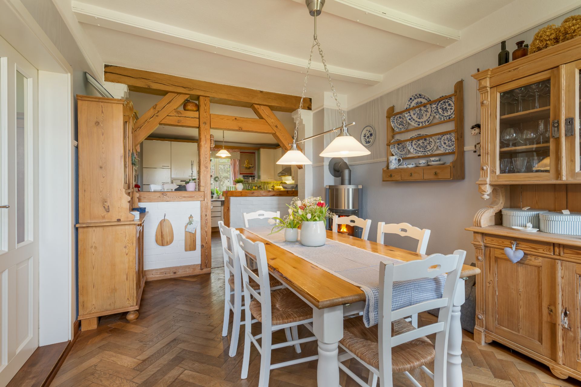 Esszimmer mit Holztisch, sechs Stühlen und rustikalen Holzmöbeln, im Hintergrund offene Küche.