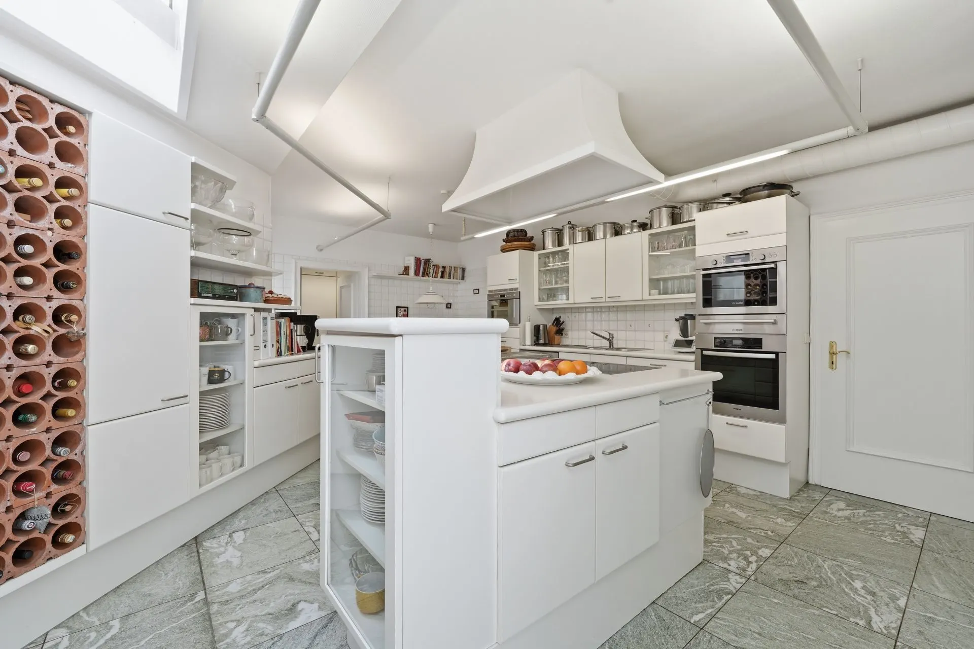 Moderne weiße Küche mit Kochinsel, Einbauschränken und Weinregal.
