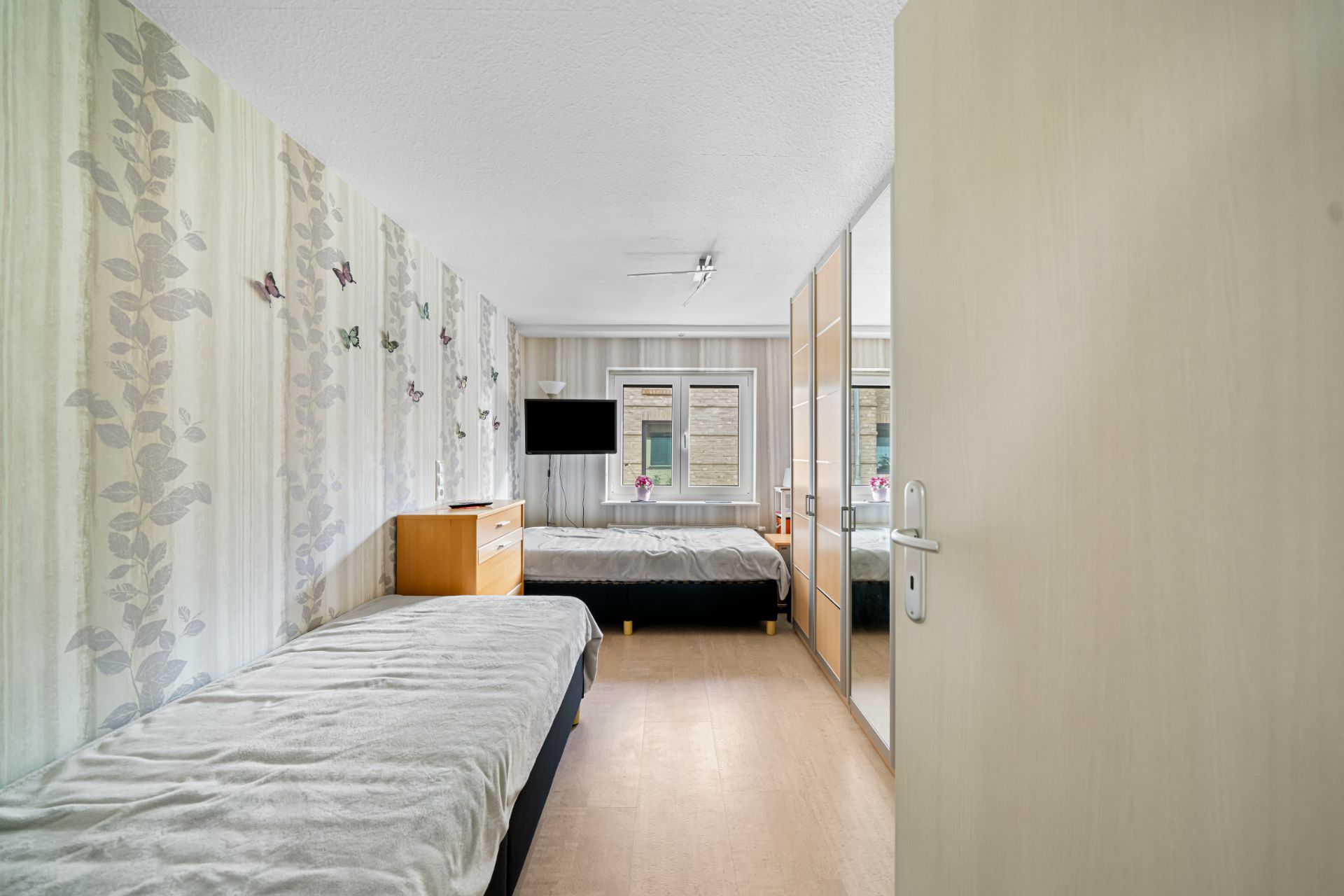 Schlafzimmer mit zwei Betten, Kleiderschrank, Kommode und Fernseher an der Wand.