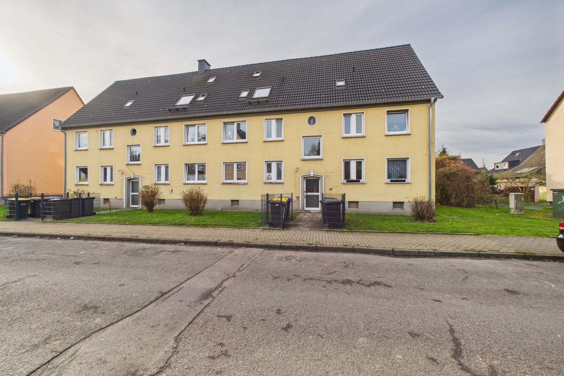 Gelbes Mehrfamilienhaus mit vielen Fenstern und Rasenflächen davor, an einer ruhigen Straße gelegen.
