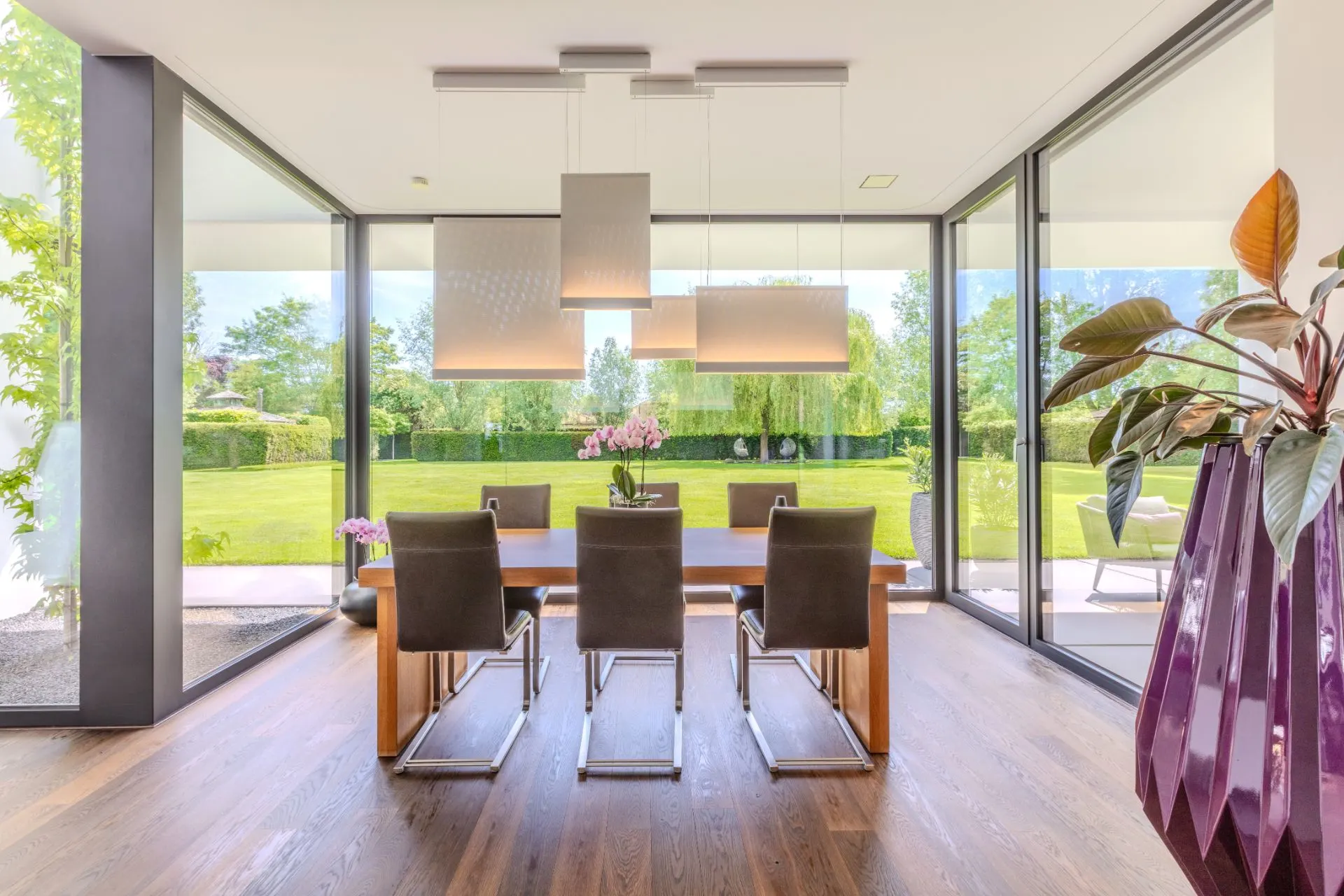 Modernes Esszimmer mit Holztisch, sechs Stühlen und großen Fenstern zum Garten.