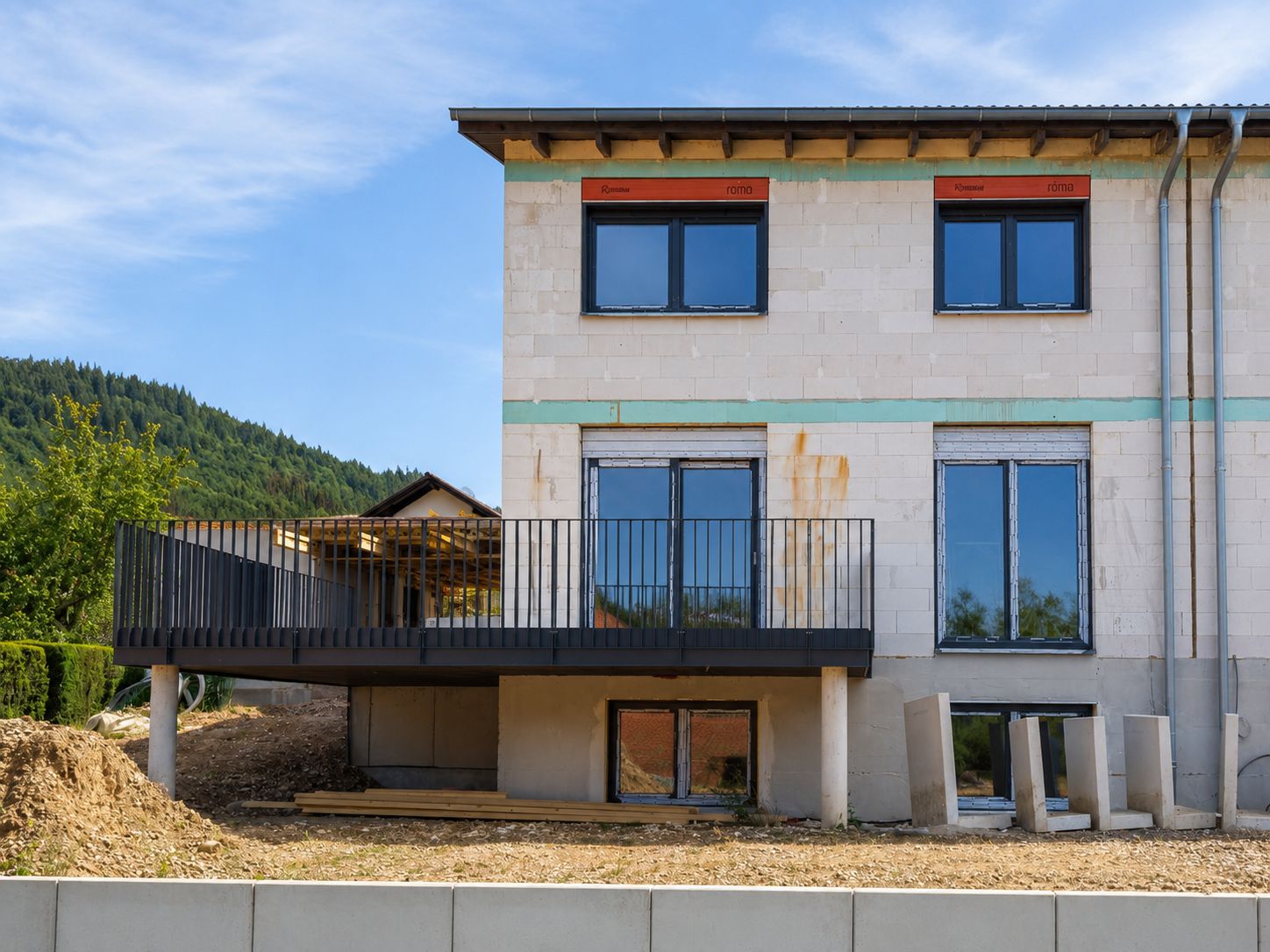 Rohbau eines zweistöckigen Wohnhauses mit Balkon und großen Fenstern.