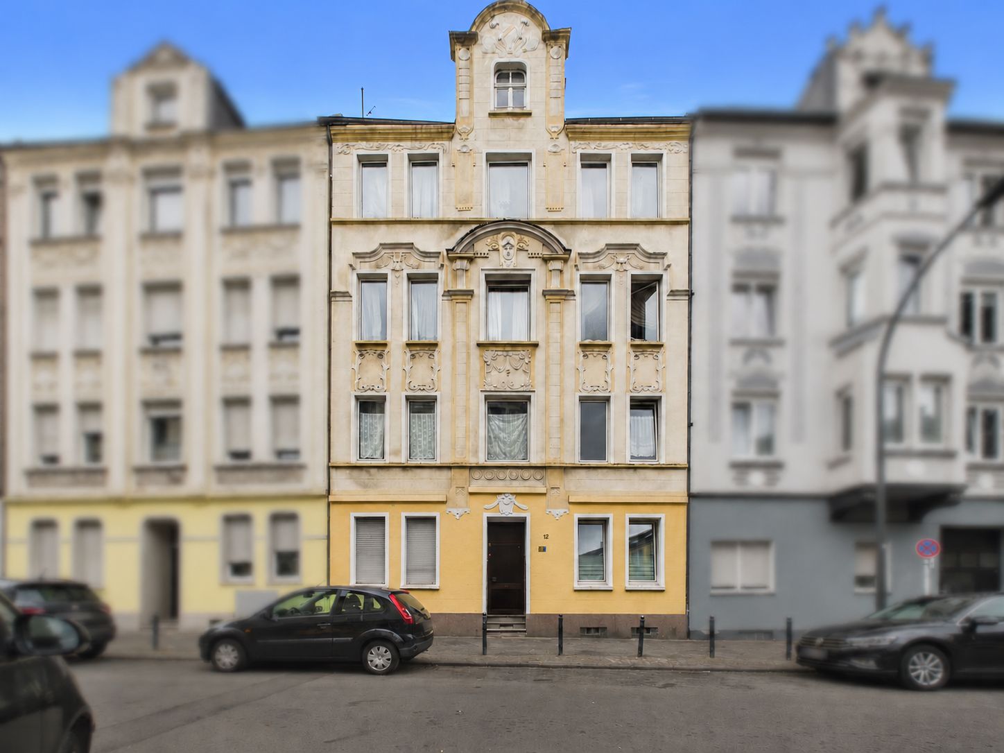 Mehrstöckiges Wohnhaus mit gelber Fassade und mehreren Fenstern, Autos parken davor.