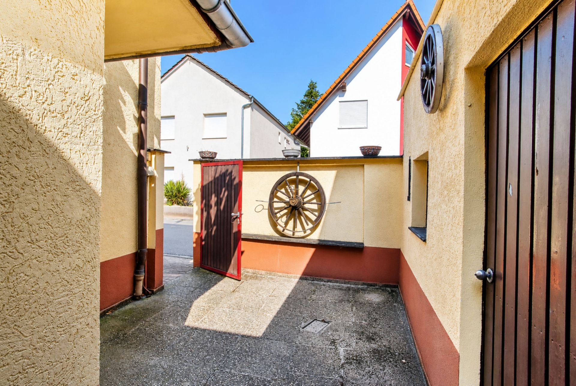 Kleiner Innenhof mit gelber Wand, Holztür und Wagenrad an der Wand.