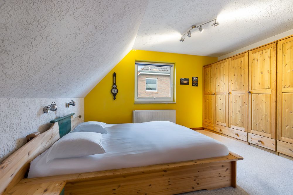 Schlafzimmer mit Doppelbett, gelber Wand, Fenster und großen Holzschränken.