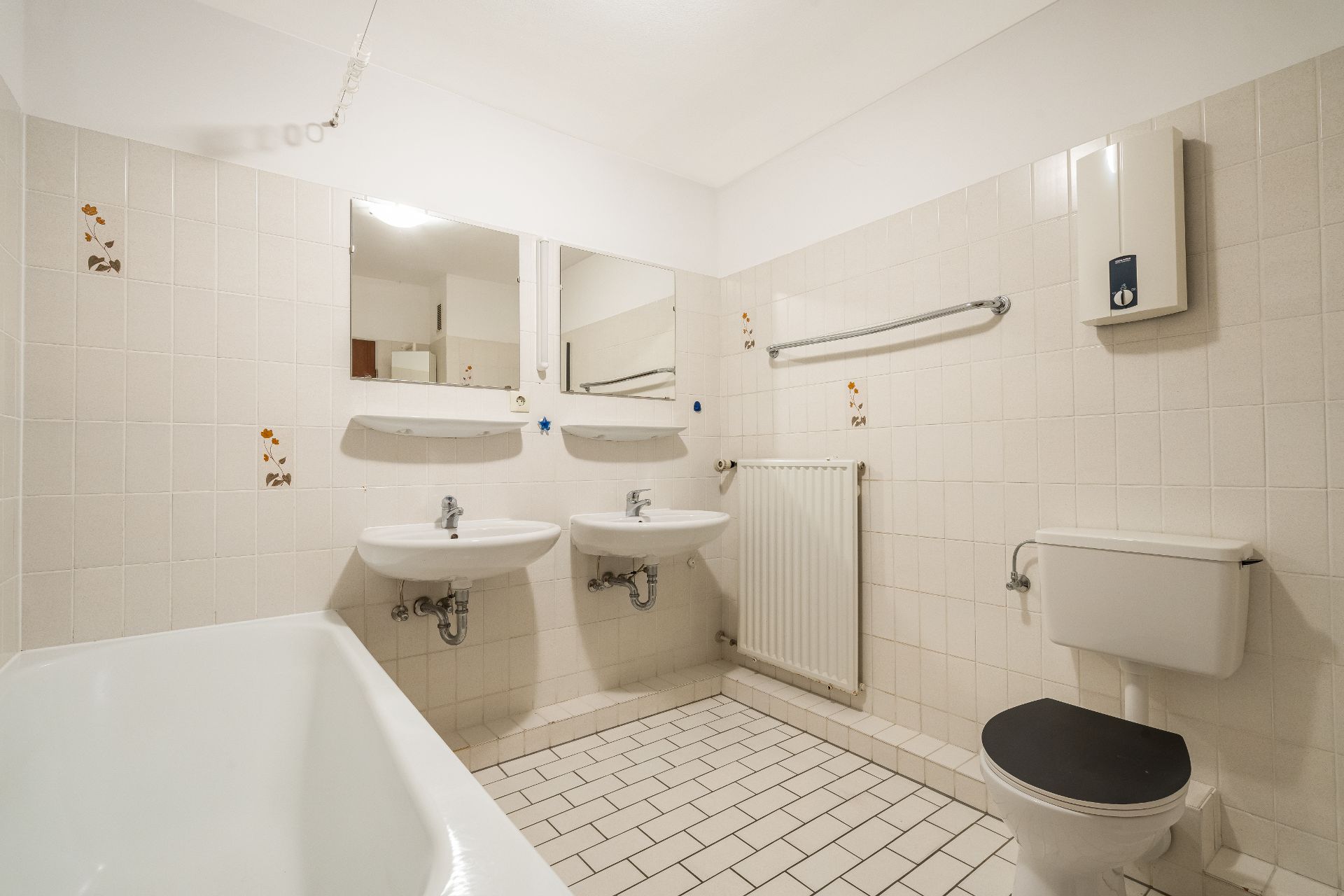 Helles Badezimmer mit zwei Waschbecken, Badewanne und Toilette, weiße Fliesen und Spiegel.