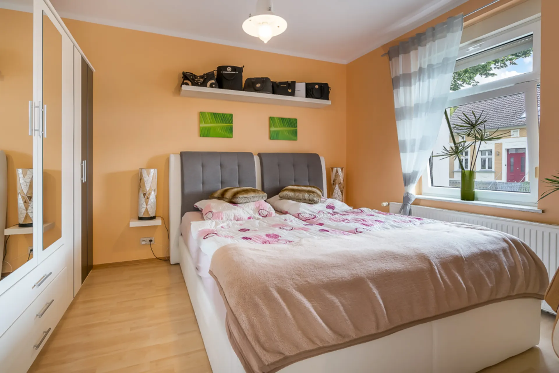 Helles Schlafzimmer mit Doppelbett, Kleiderschrank, Fenster und Dekorationen an der Wand.