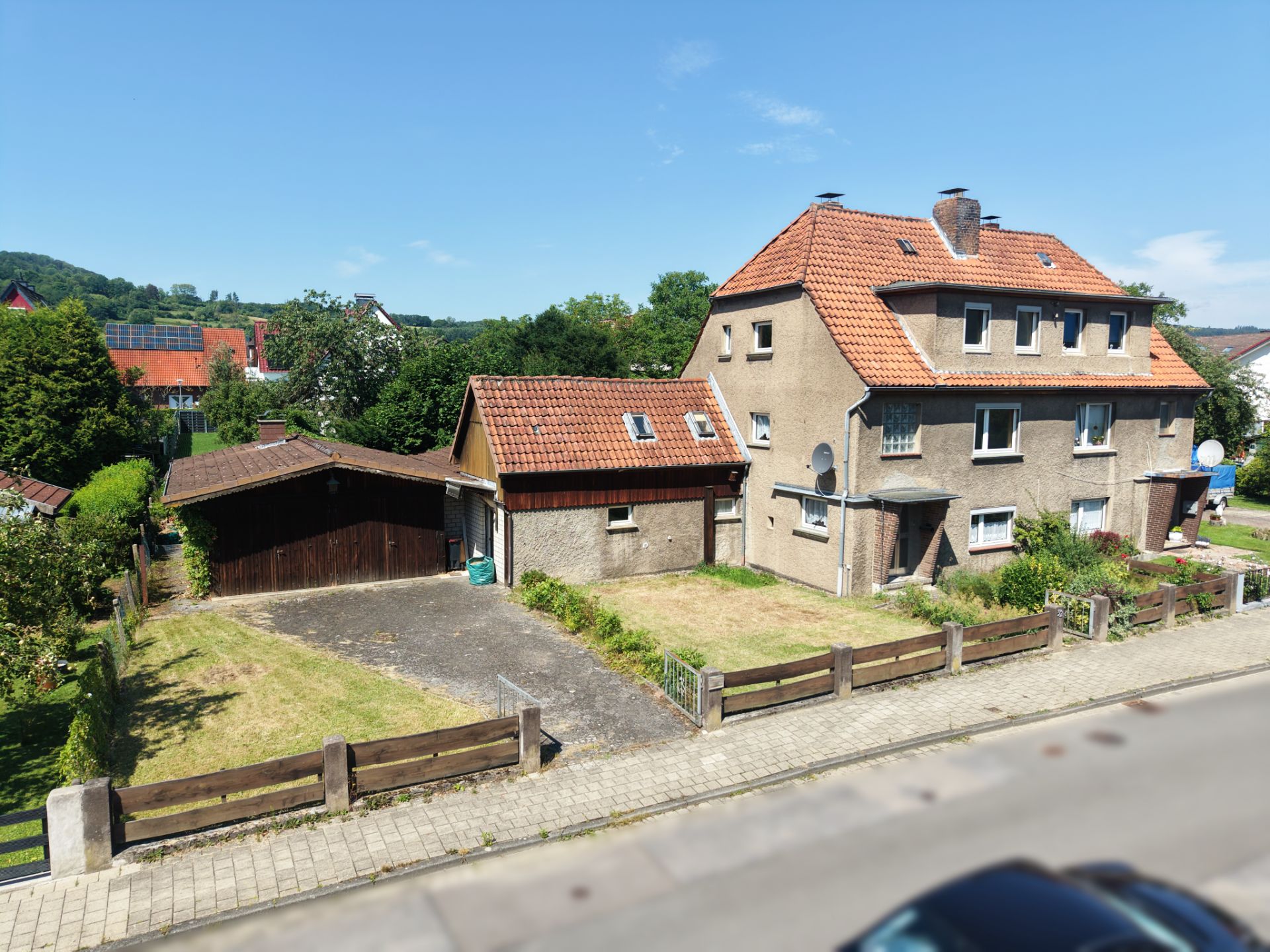 Zweistöckiges Wohnhaus mit rotem Dach, Garage und kleinem Vorgarten an einer Straße.