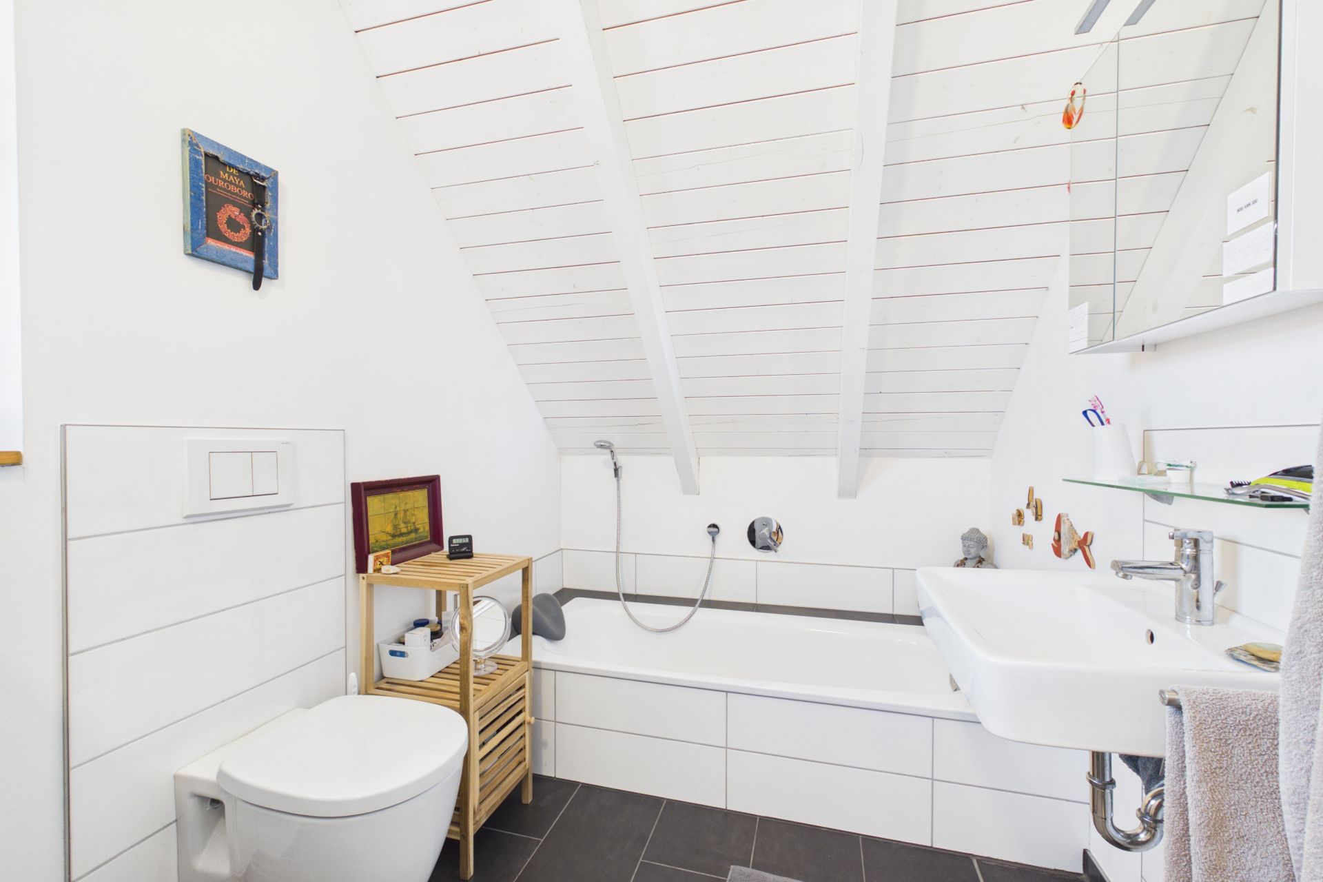 Helles Bad mit Badewanne, WC, Waschbecken und Regal unter einer Dachschräge.