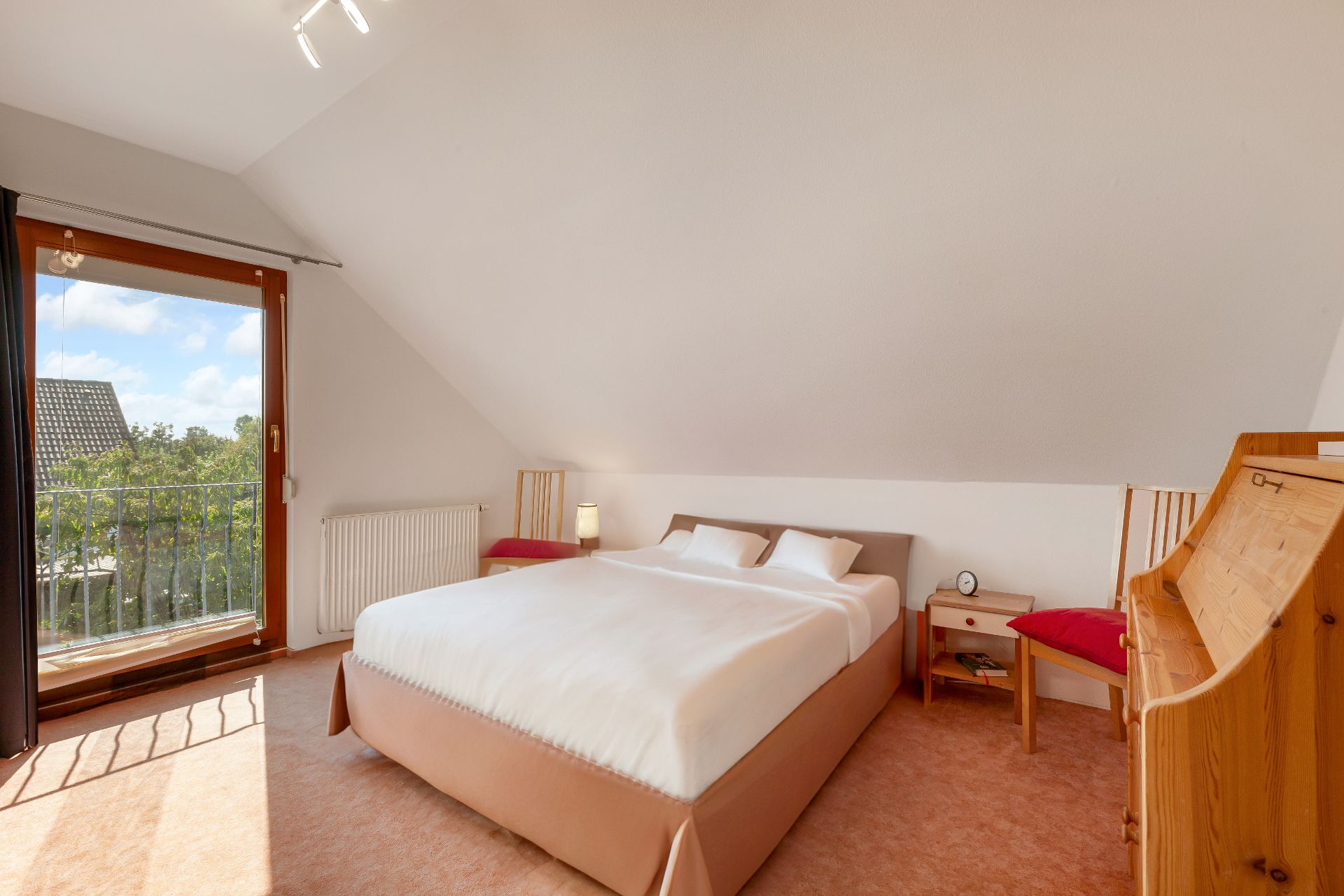 Helles Schlafzimmer mit Doppelbett, zwei Stühlen, Nachttisch und Schreibtisch unter Dachschräge.