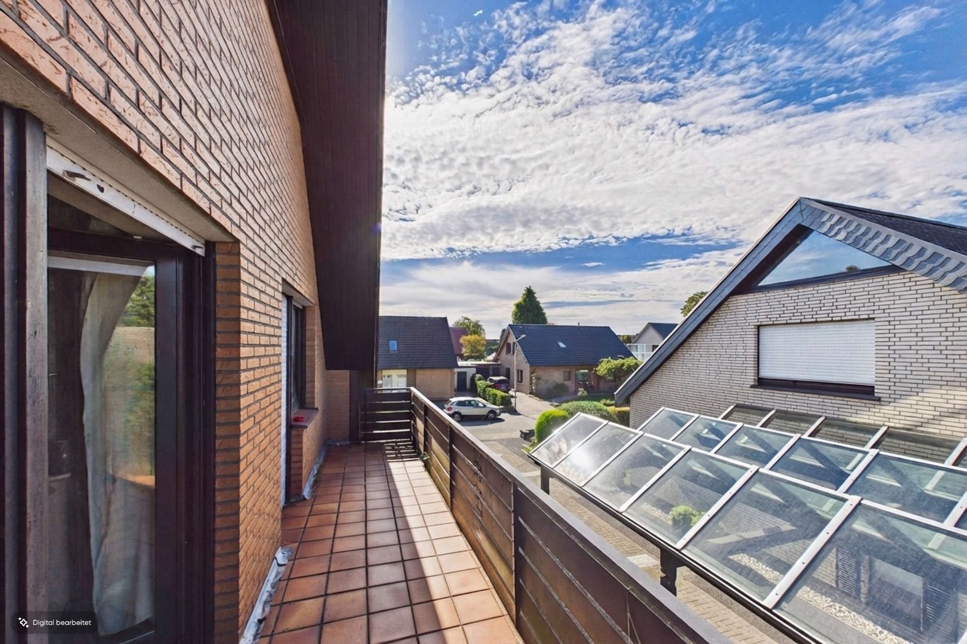 Balkon mit braunen Fliesen, Blick auf Wohnhäuser und verglasten Carport bei sonnigem Wetter.