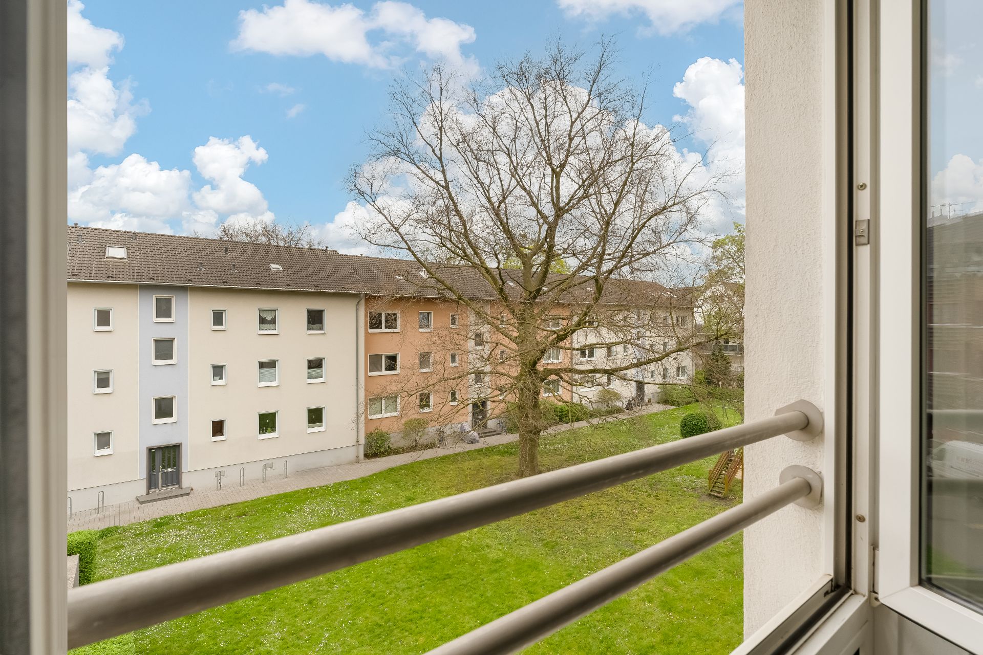 Blick aus dem Fenster auf einen grünen Innenhof mit Bäumen und Wohngebäuden.
