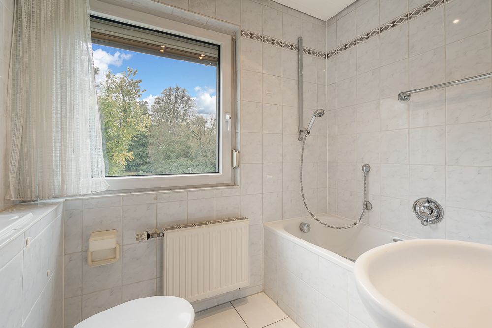 Helles Badezimmer mit Fenster, Badewanne, Dusche, Waschbecken und Toilette.