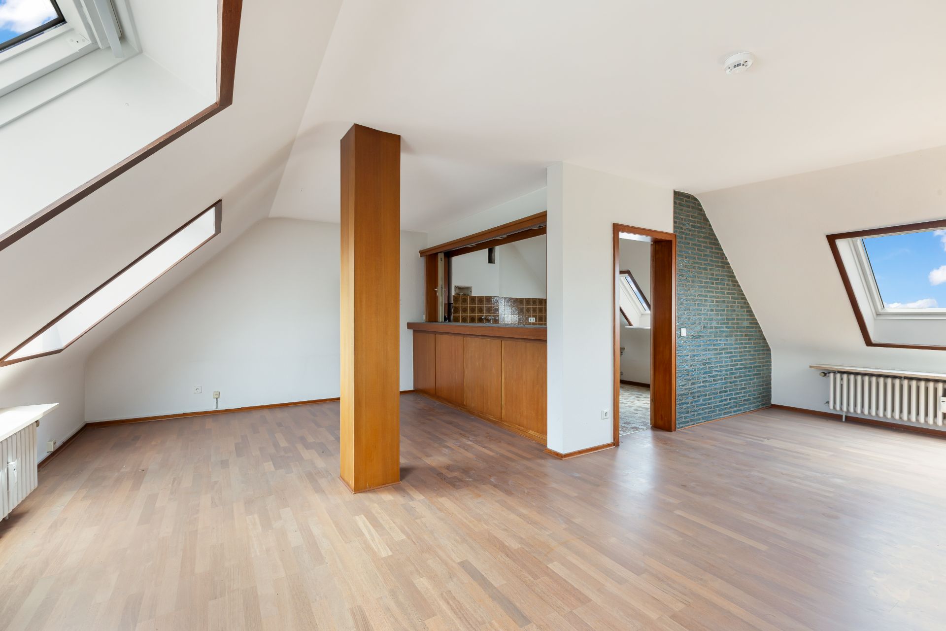 Helles Dachgeschoss mit Holzfußboden, offenen Fenstern und einer offenen Küche.