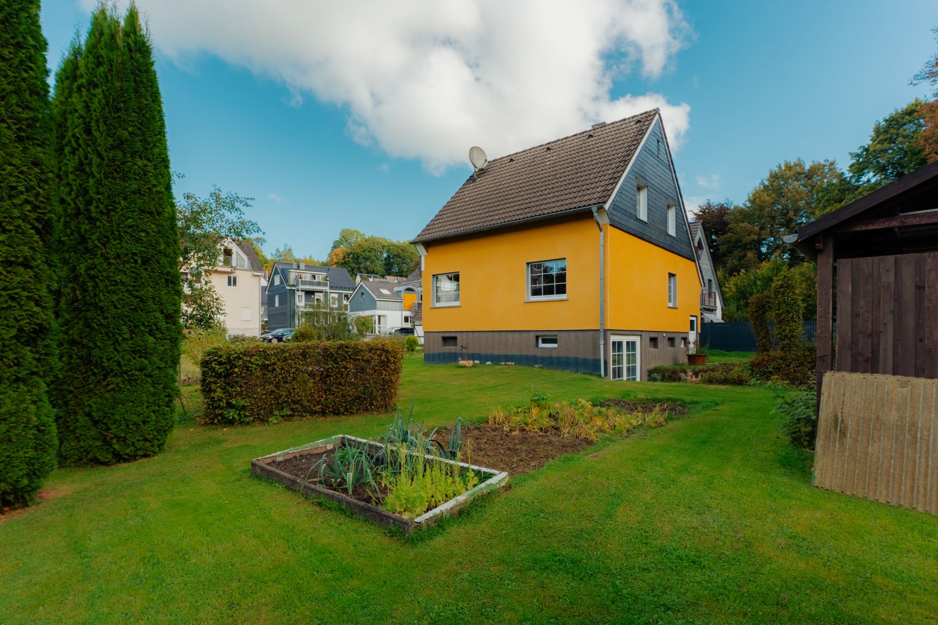 Gelbes Einfamilienhaus mit Garten, kleinem Gemüsebeet und Rasenfläche.