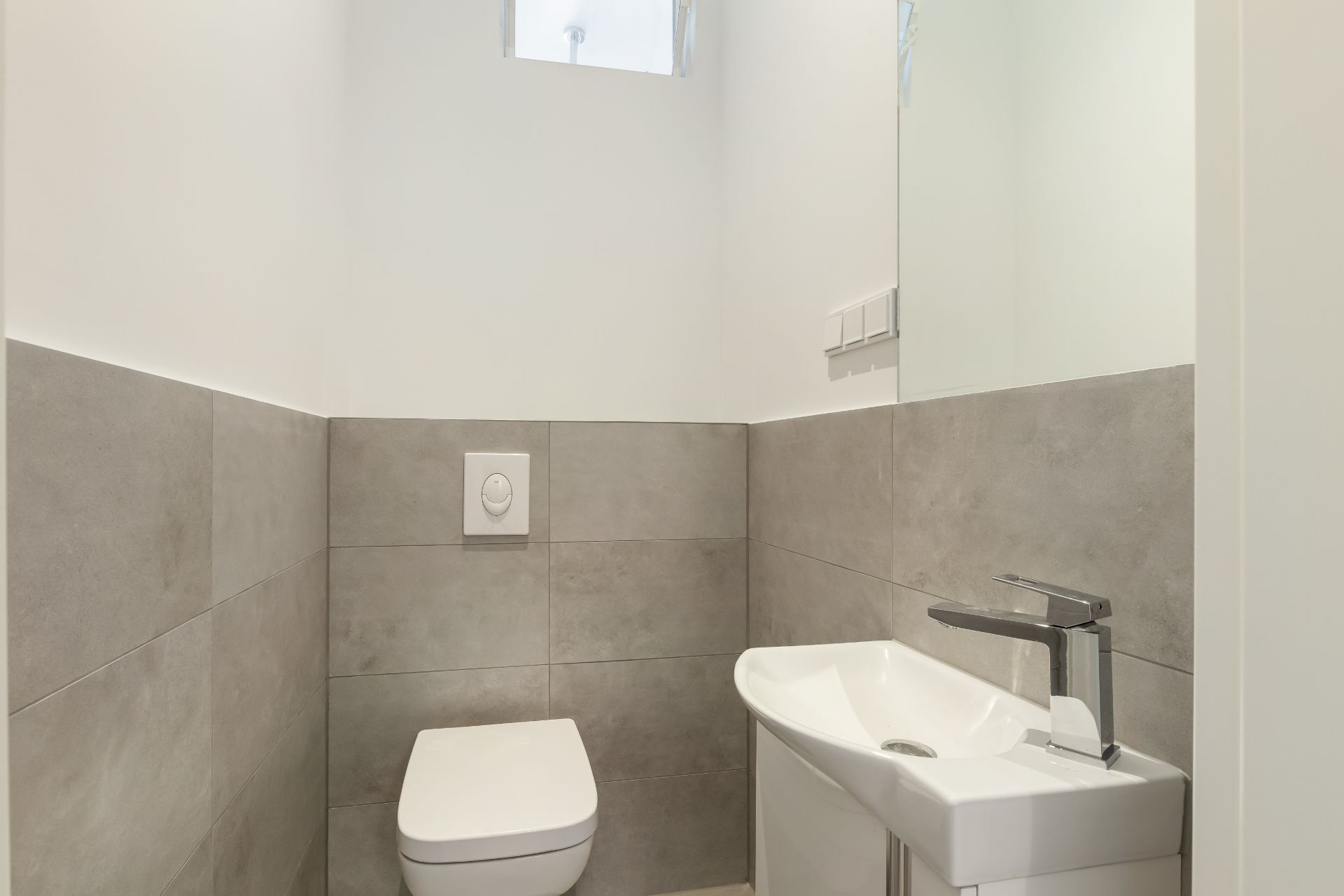 Modernes kleines WC mit Hänge-WC, kleinem Waschbecken und grauen Fliesen.