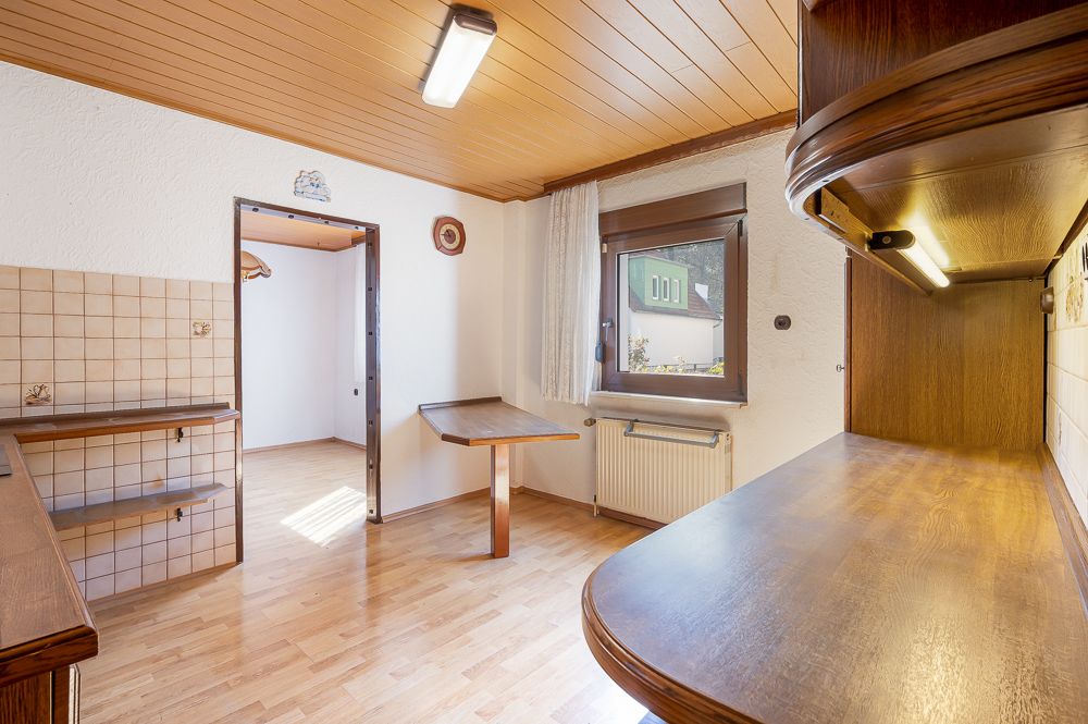 Helle Küche mit Holzboden, Holzdecke und großem Fenster, klappbarem Tisch und offenen Regalen.