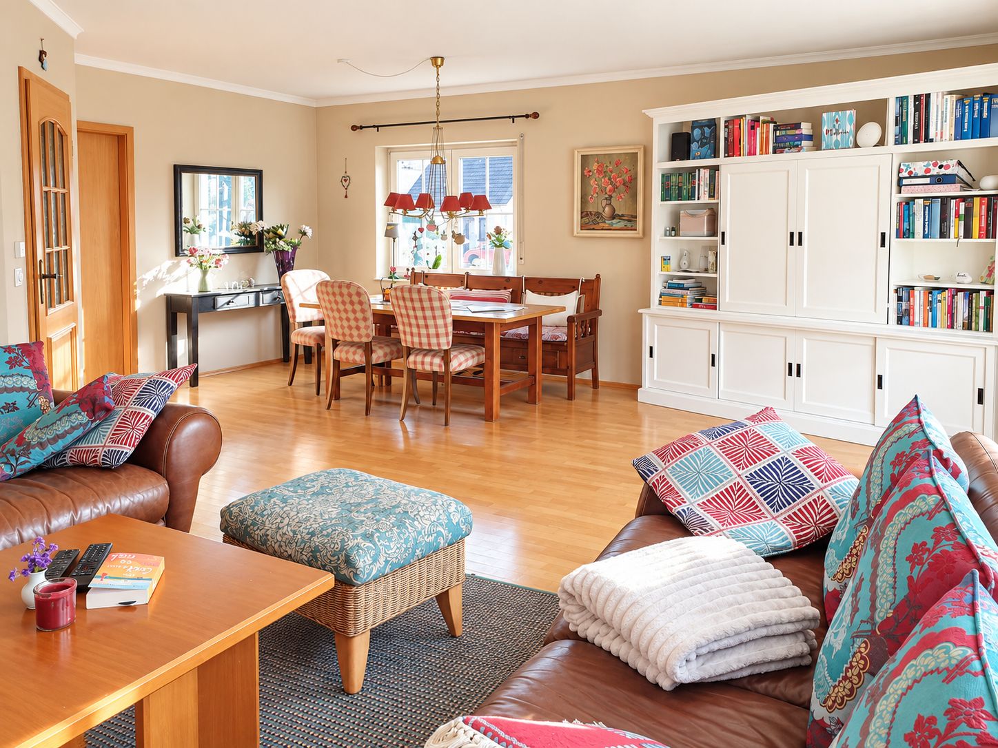 Helles Wohnzimmer mit Ledersofas, Esstisch, Bücherregal und Holzfußboden.