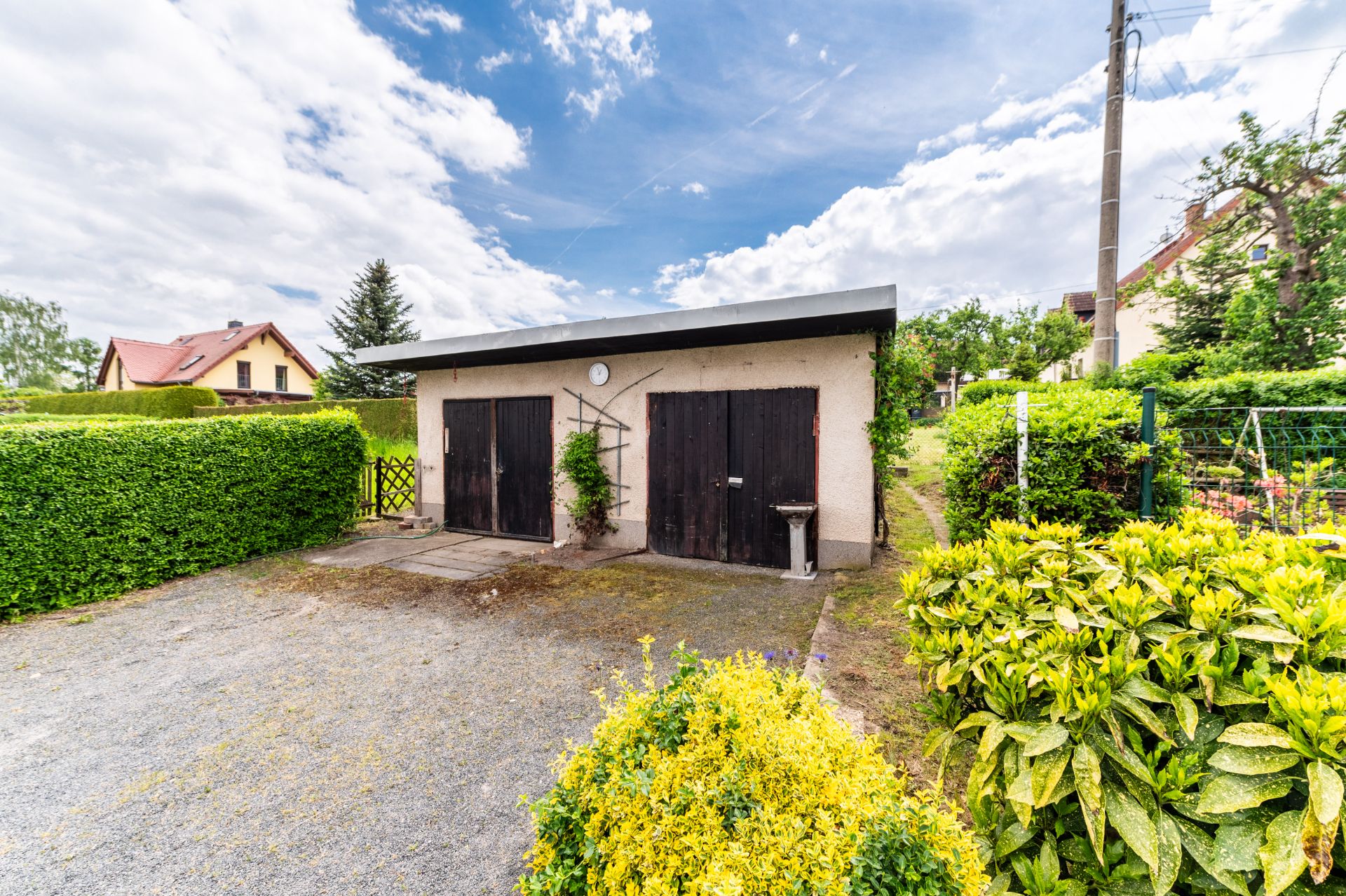 Zweckbau mit zwei Holztoren, umgeben von Hecken und Pflanzen im Vorgarten.