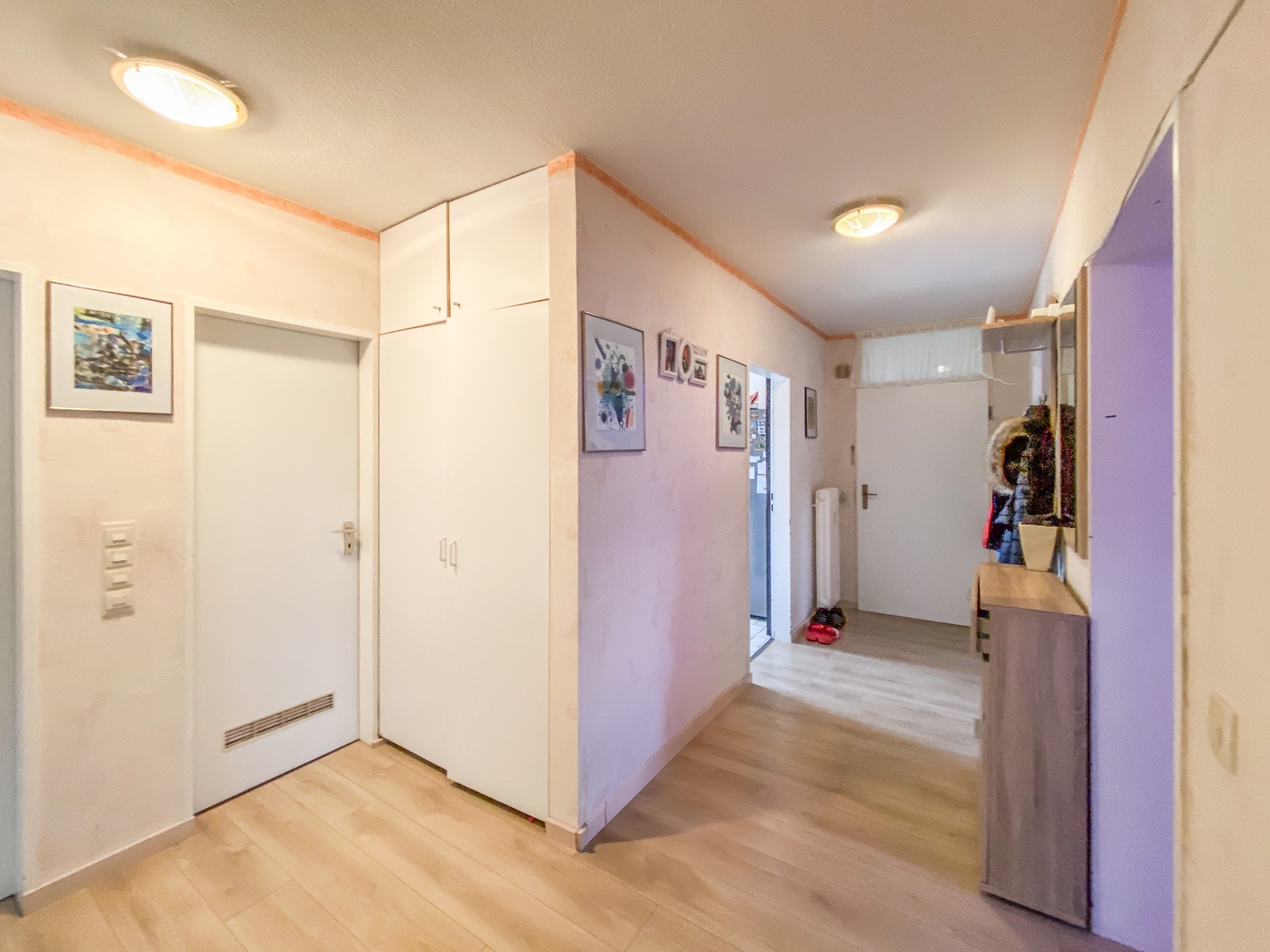 Heller Flur mit Holzfußboden, weißen Türen, Schränken und Bildern an den Wänden.