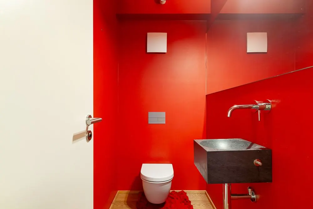 Kleines Gäste-WC mit roter Wandfarbe, Wandtoilette, schwarzem Waschbecken und Spiegel.
