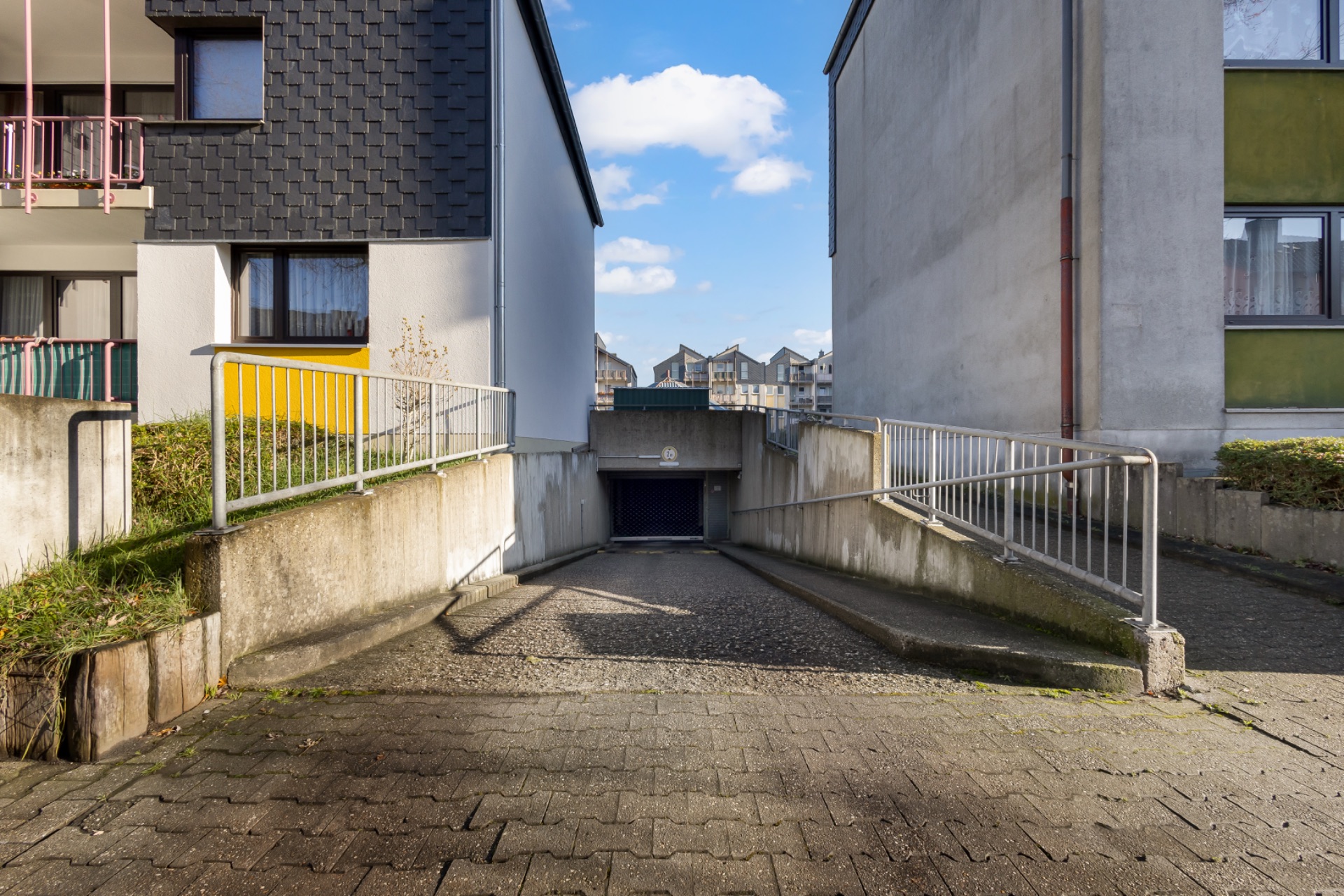 Einfahrt zu einer Tiefgarage zwischen zwei Wohngebäuden bei Tageslicht.