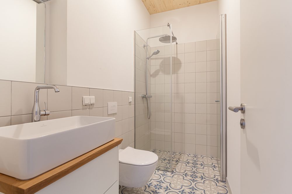 Modernes Badezimmer mit Waschbecken, Toilette, Duschkabine und gemustertem Fliesenboden.
