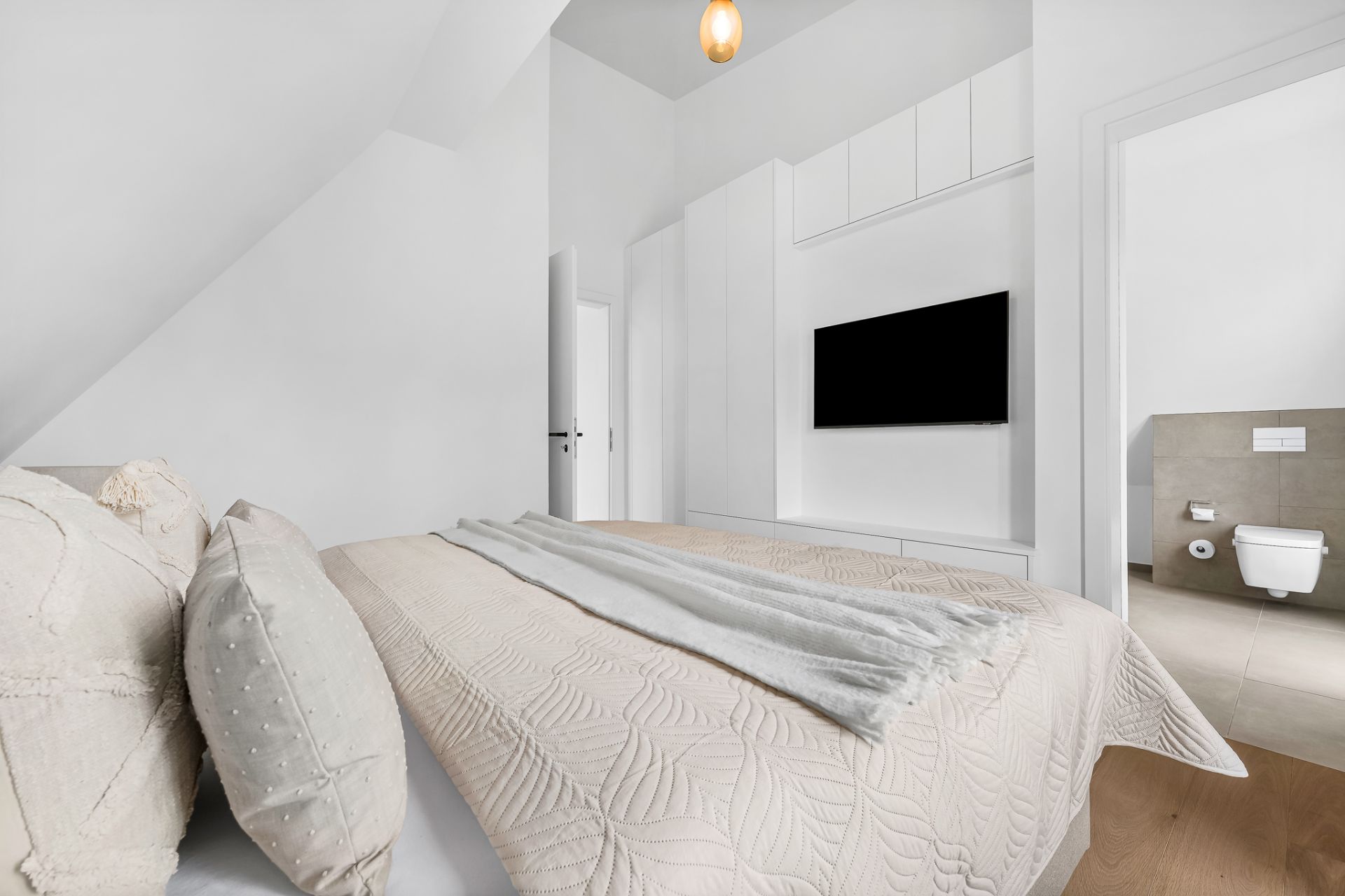 Helles Schlafzimmer mit Doppelbett, TV, Kleiderschrank und Zugang zu einem Badezimmer.