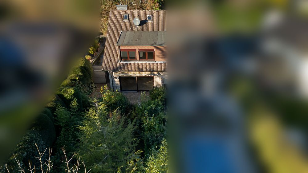 Zweistöckiges Haus mit Satteldach, großen Fenstern und umgeben von viel Grün.