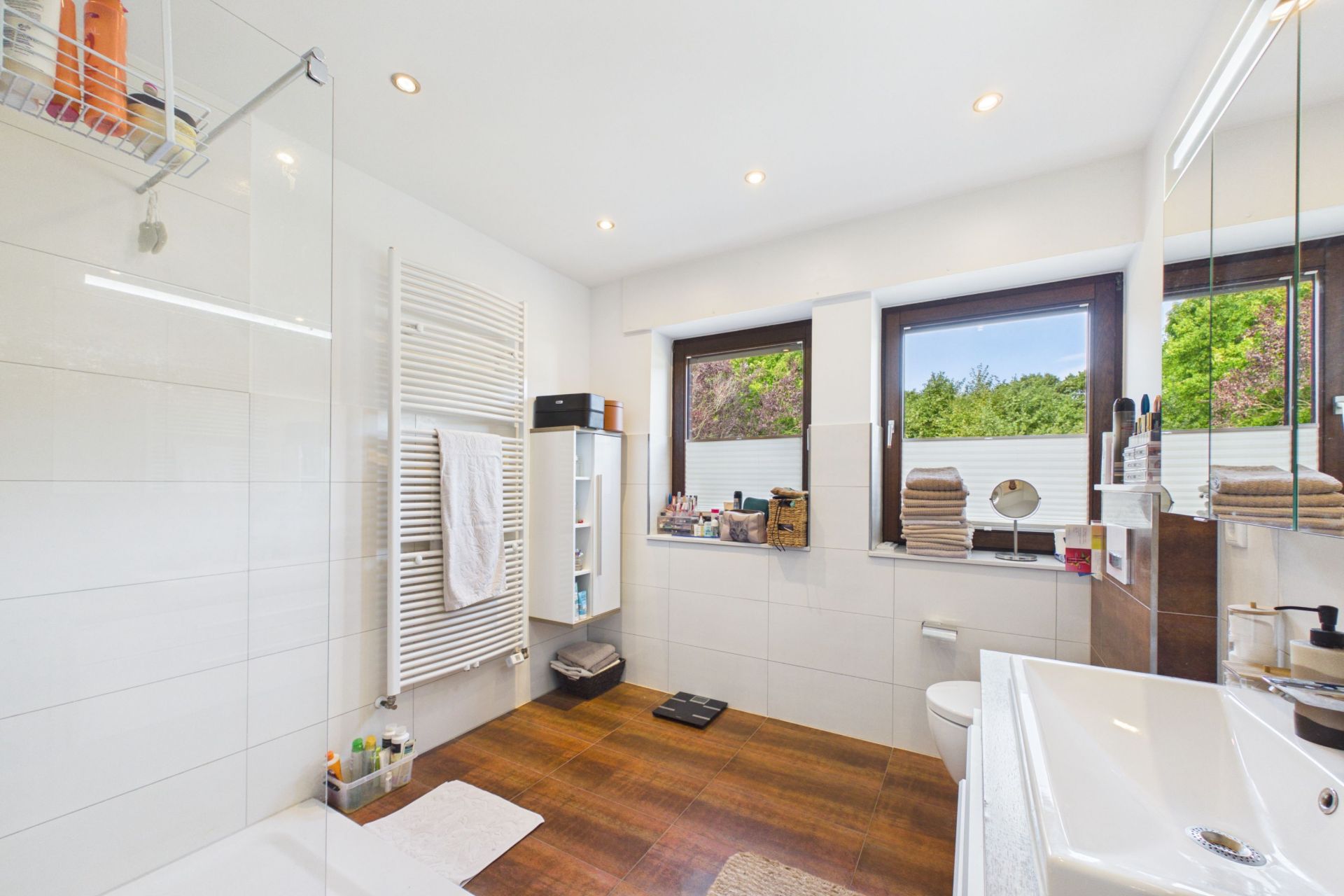 Modernes Badezimmer mit zwei Fenstern, Dusche, Waschbecken, WC und Handtuchheizkörper.