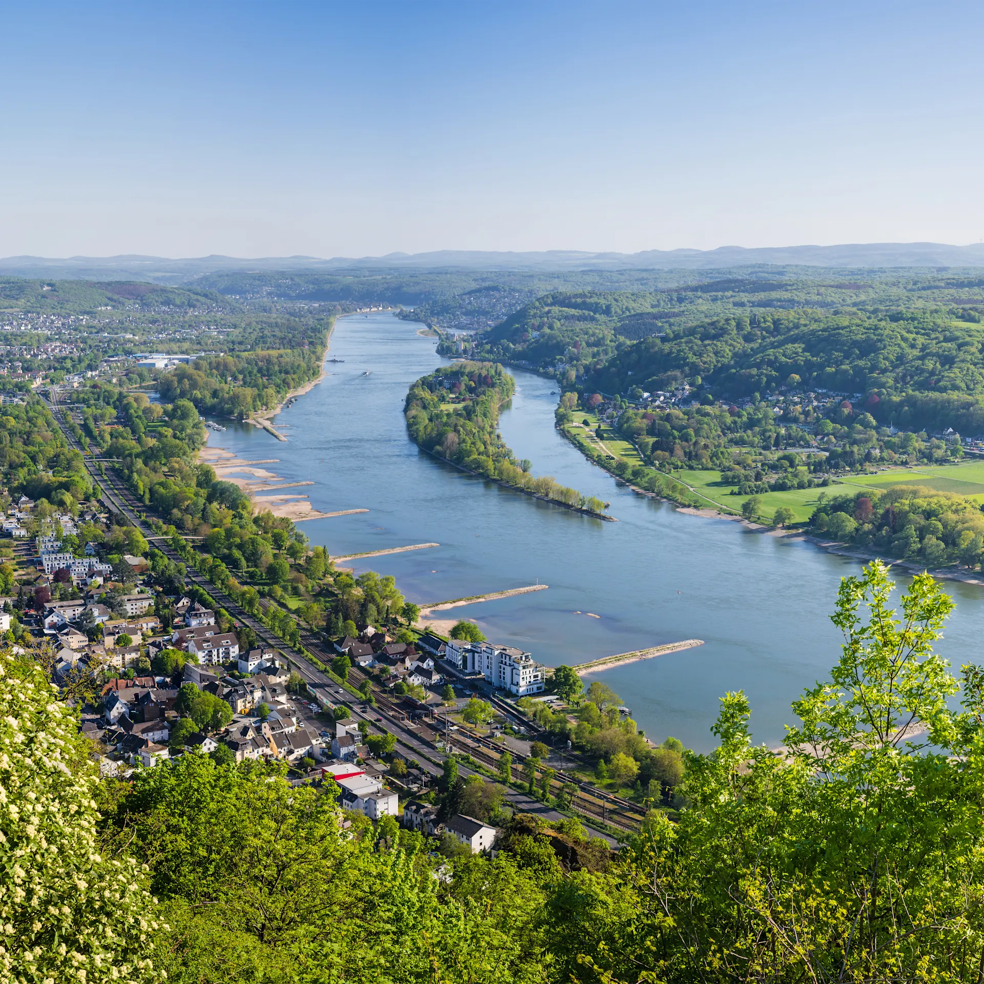 Blick von oben auf einen breiten Fluss, umgeben von grünen Hügeln und Wohnhäusern.