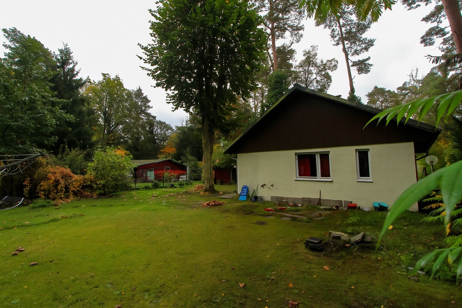 Ein kleines Haus mit Garten und Bäumen, daneben stehen Gartenstühle und Spielzeug auf der Wiese.