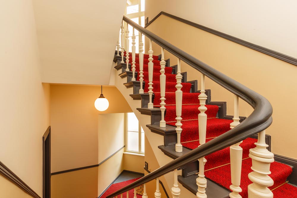 Treppe mit rotem Teppich und weißem Geländer in einem Wohnhaus.
