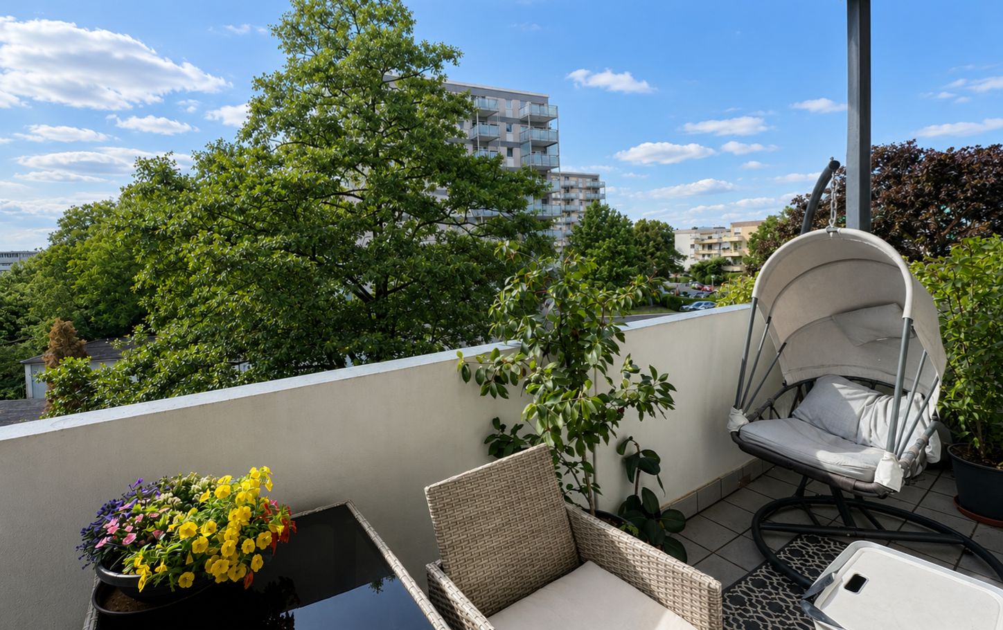 Balkon mit Stuhl, Hängesessel, Pflanzen und Blick auf Bäume und Wohngebäude.