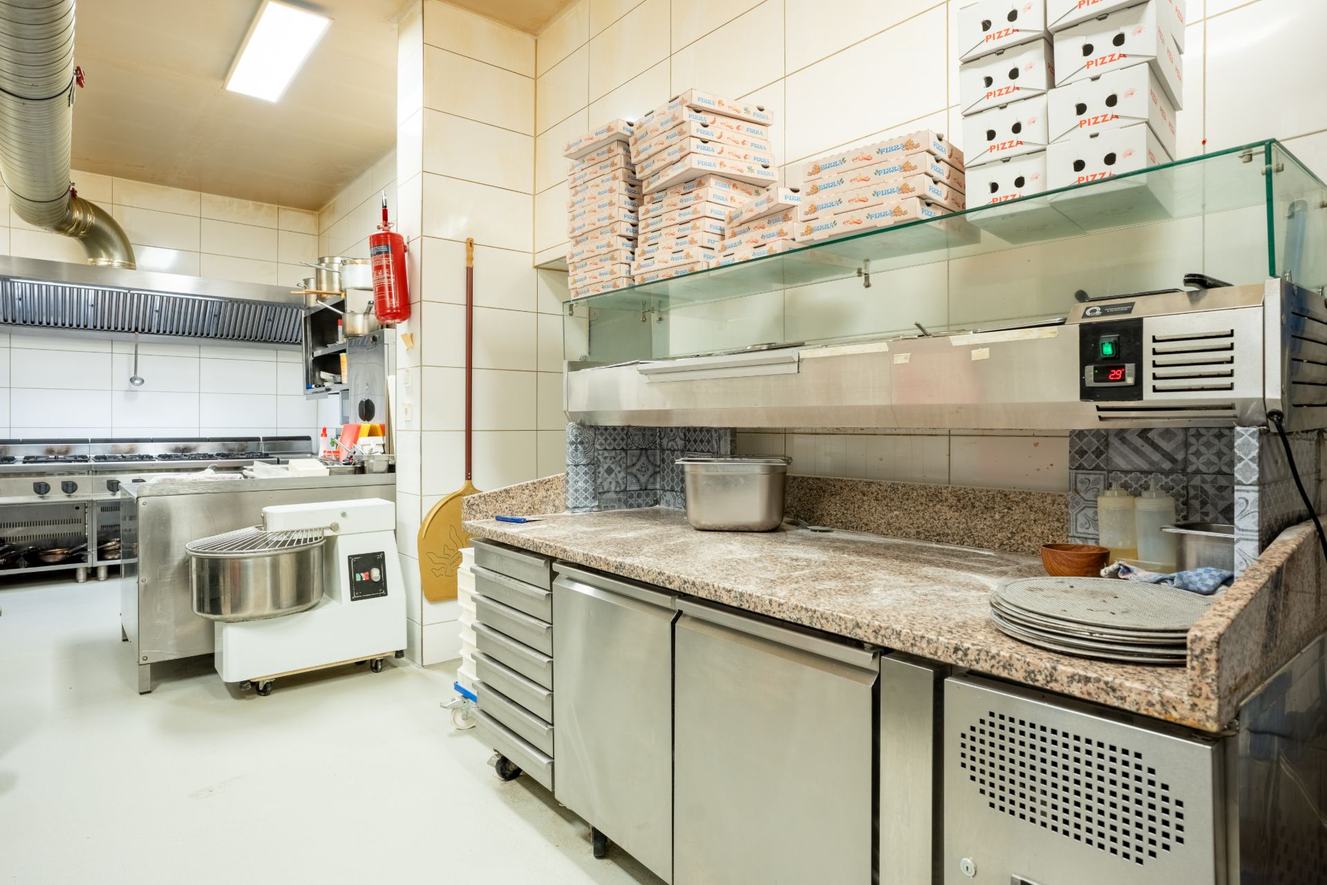 Moderne Küche mit Edelstahlgeräten, Arbeitsfläche, Pizzakartons und Küchenutensilien.