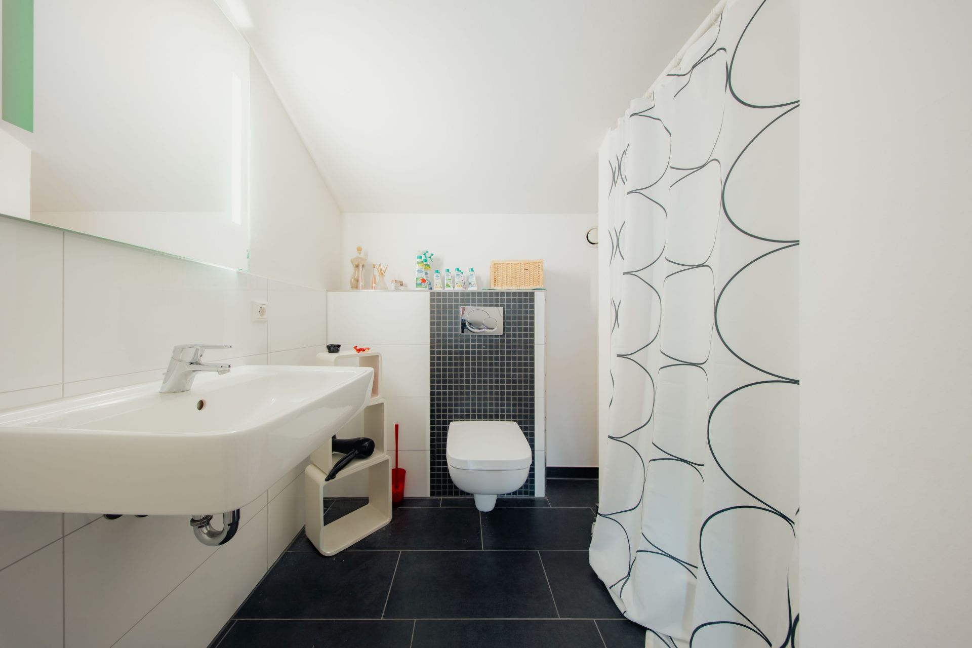 Modernes Badezimmer mit Waschbecken, WC und Dusche mit Vorhang, schwarze Bodenfliesen.