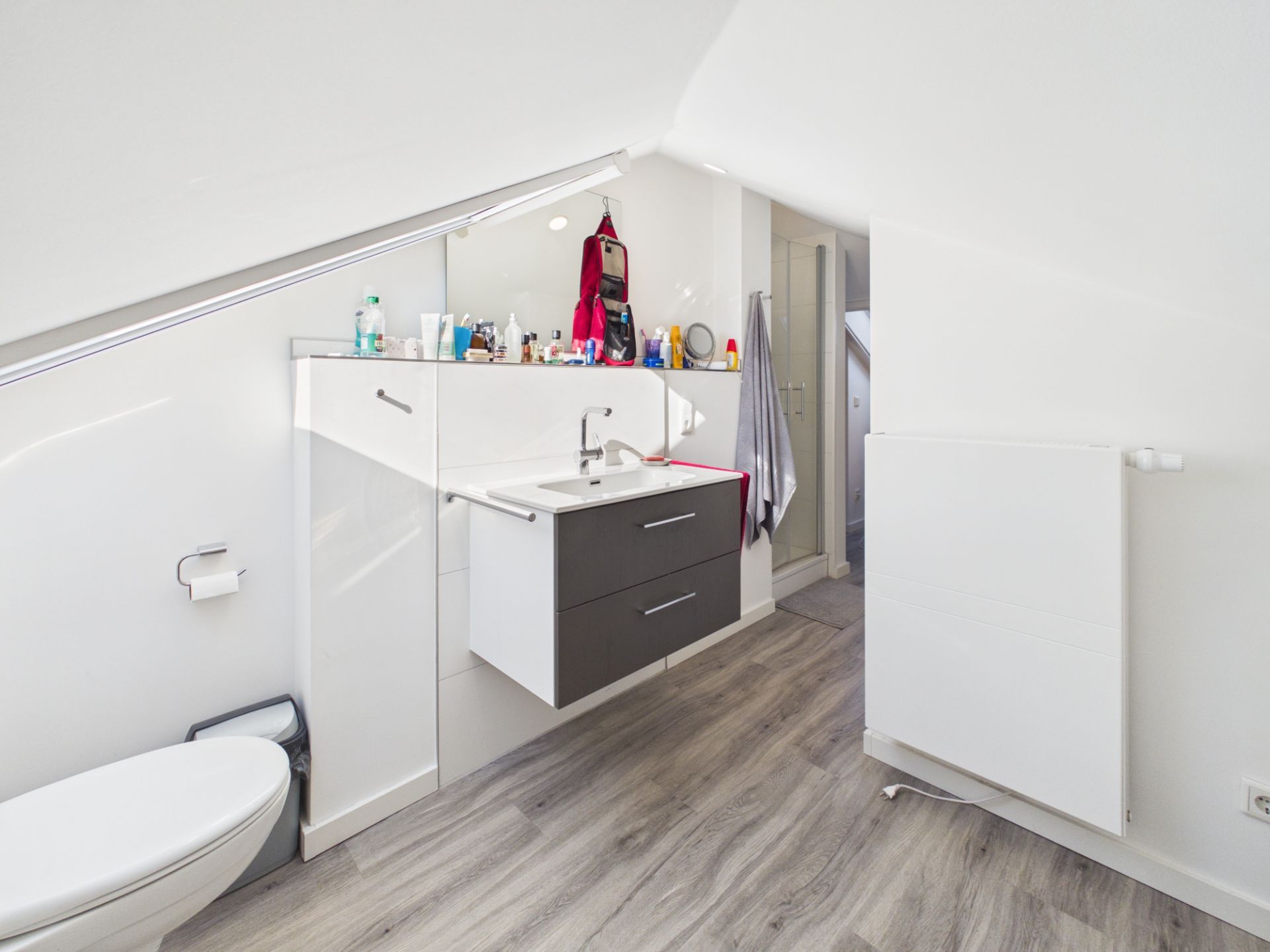 Modernes Bad mit Waschbecken, Spiegel, Toilette und Dachschräge, helle Einrichtung und Holzfußboden.