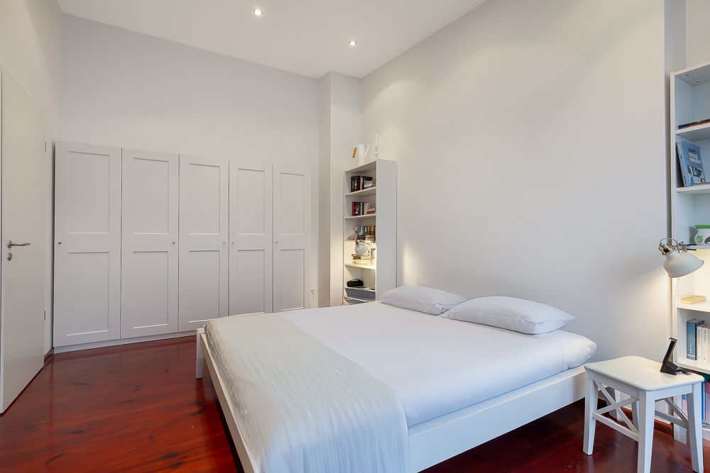 Modernes Schlafzimmer mit Doppelbett, weißen Schränken und Regalen auf Holzfußboden.