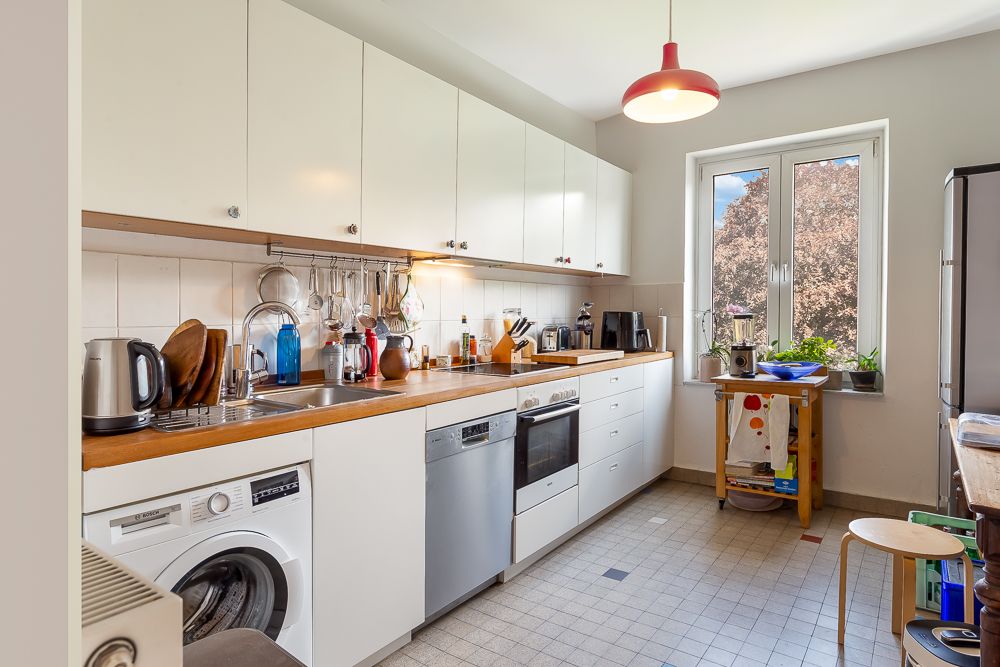 Helle Küche mit weißen Schränken, Waschmaschine, Spüle, Herd und großem Fenster.