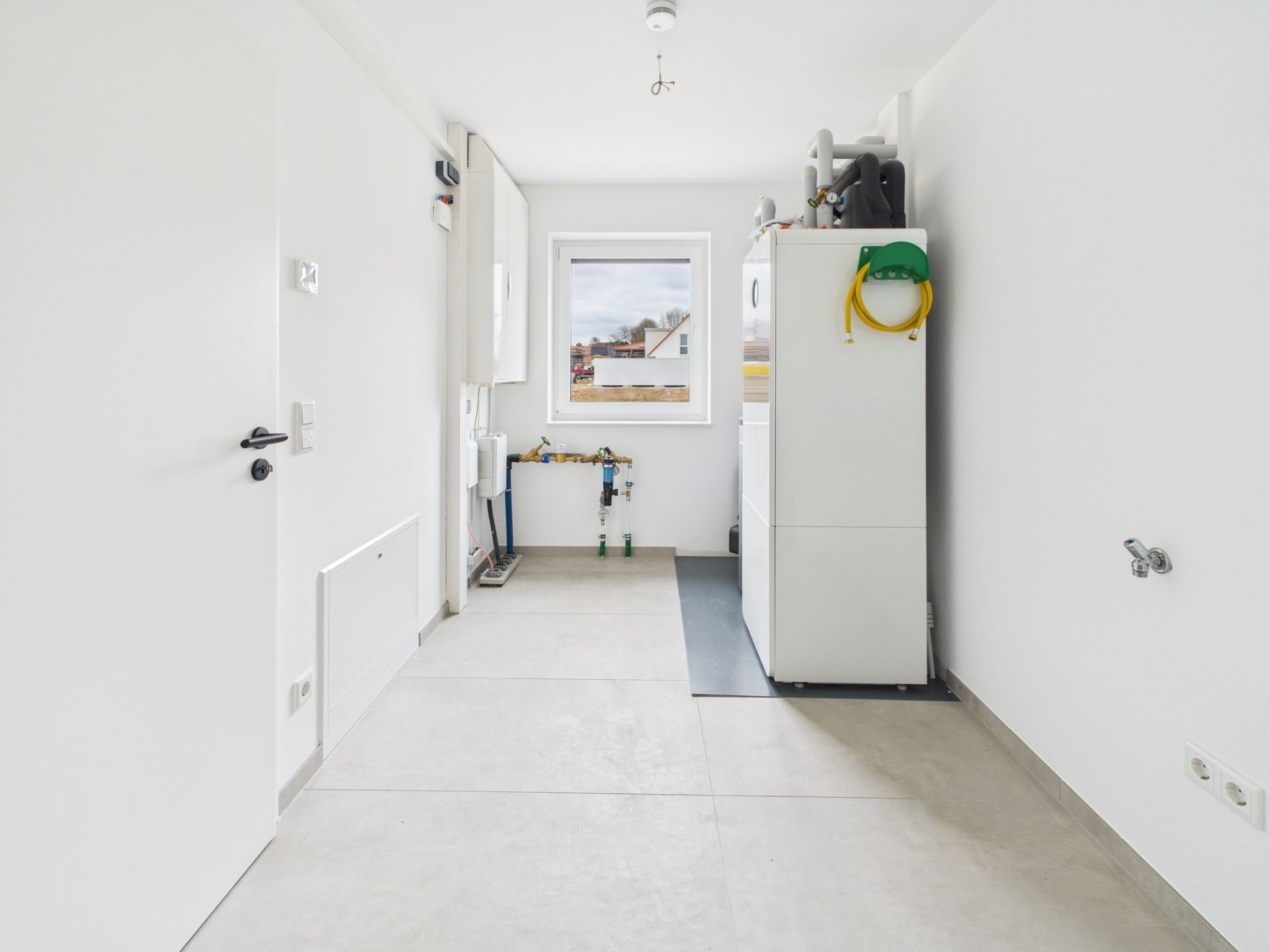 Heller Hauswirtschaftsraum mit Heizung, weißen Wänden und Fenster.