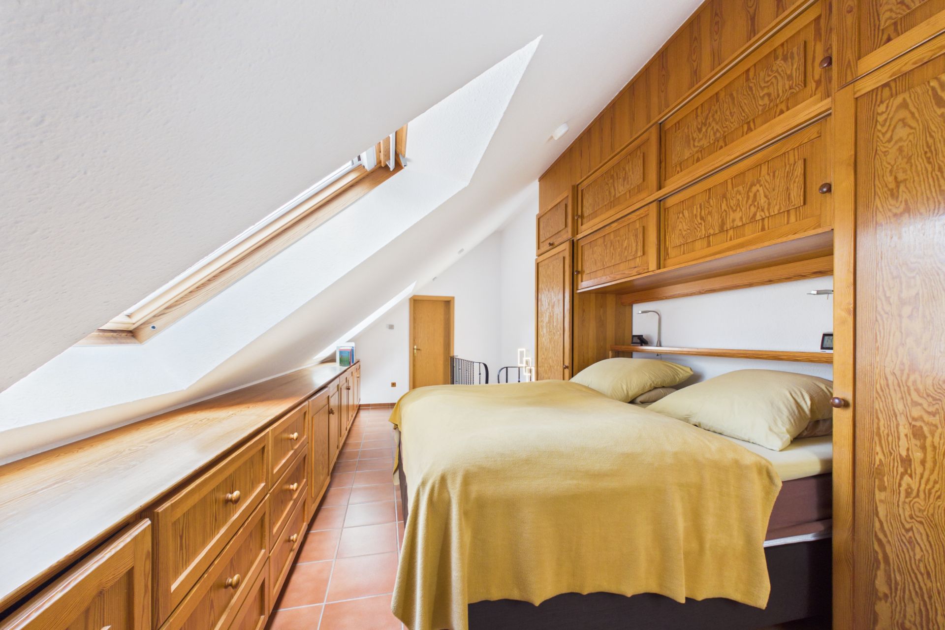 Schlafzimmer mit Dachschräge, Doppelbett und Einbauschränken aus Holz.