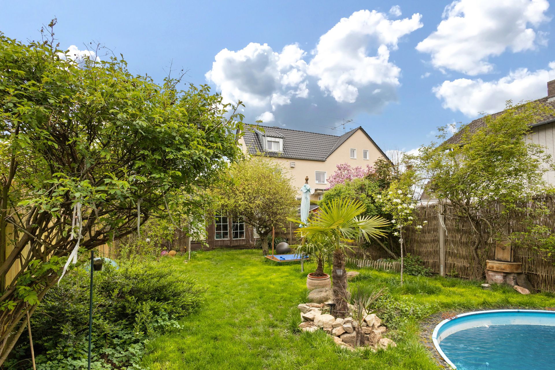 Grüner Garten mit Bäumen, kleinem Pool und Blick auf ein Haus im Hintergrund.