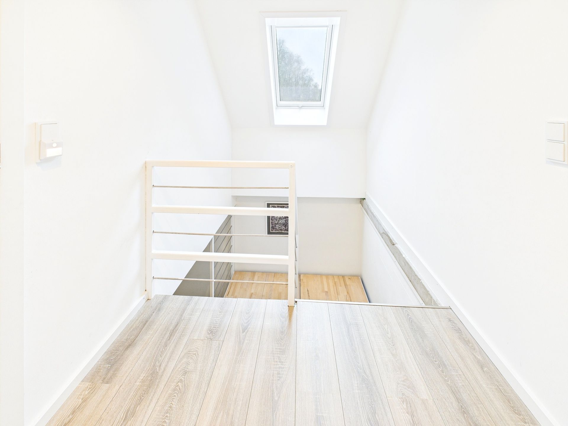 Heller Flur mit Holzfußboden, weißem Geländer und Dachfenster.