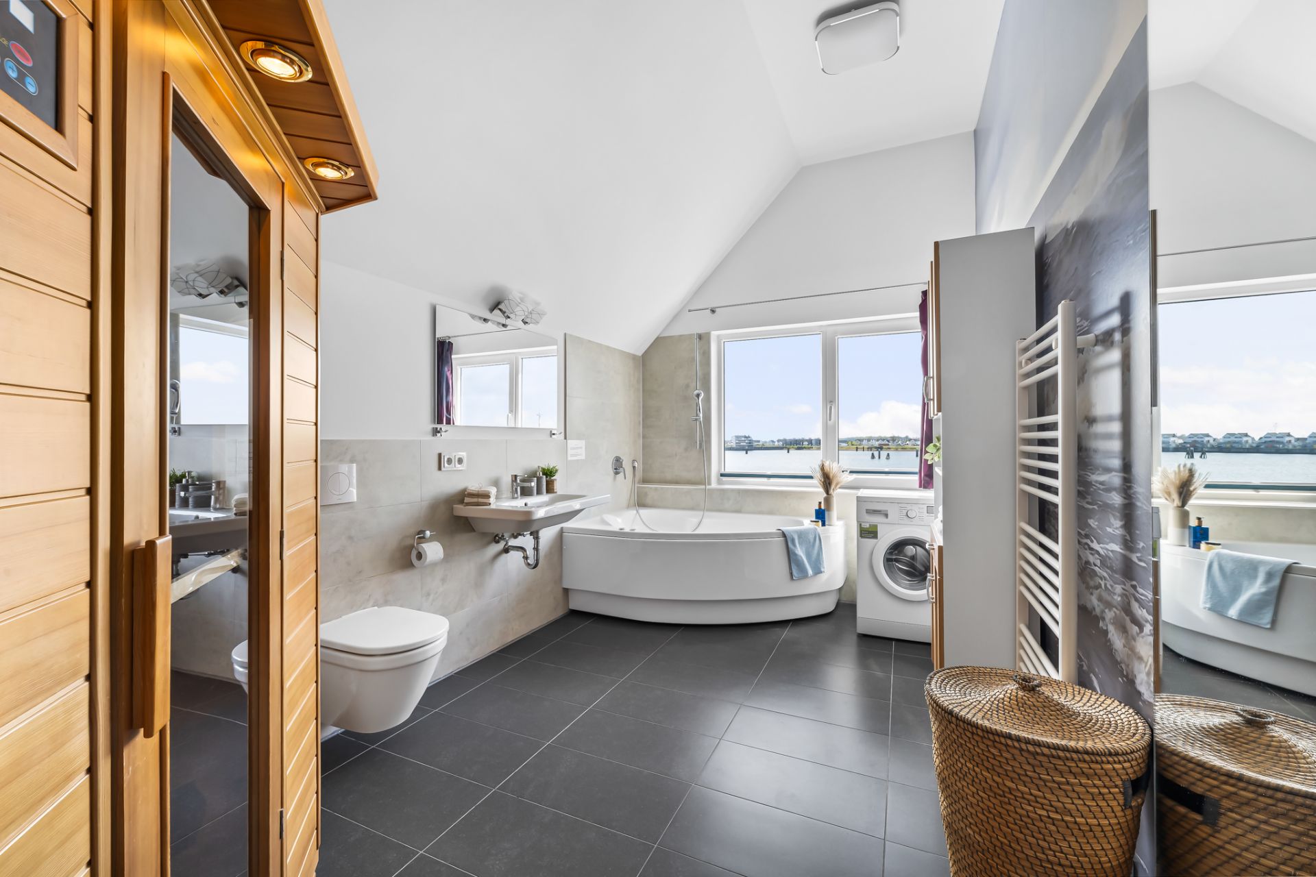 Modernes Badezimmer mit Sauna, Eckbadewanne, Waschmaschine und großen Fenstern mit Seeblick.